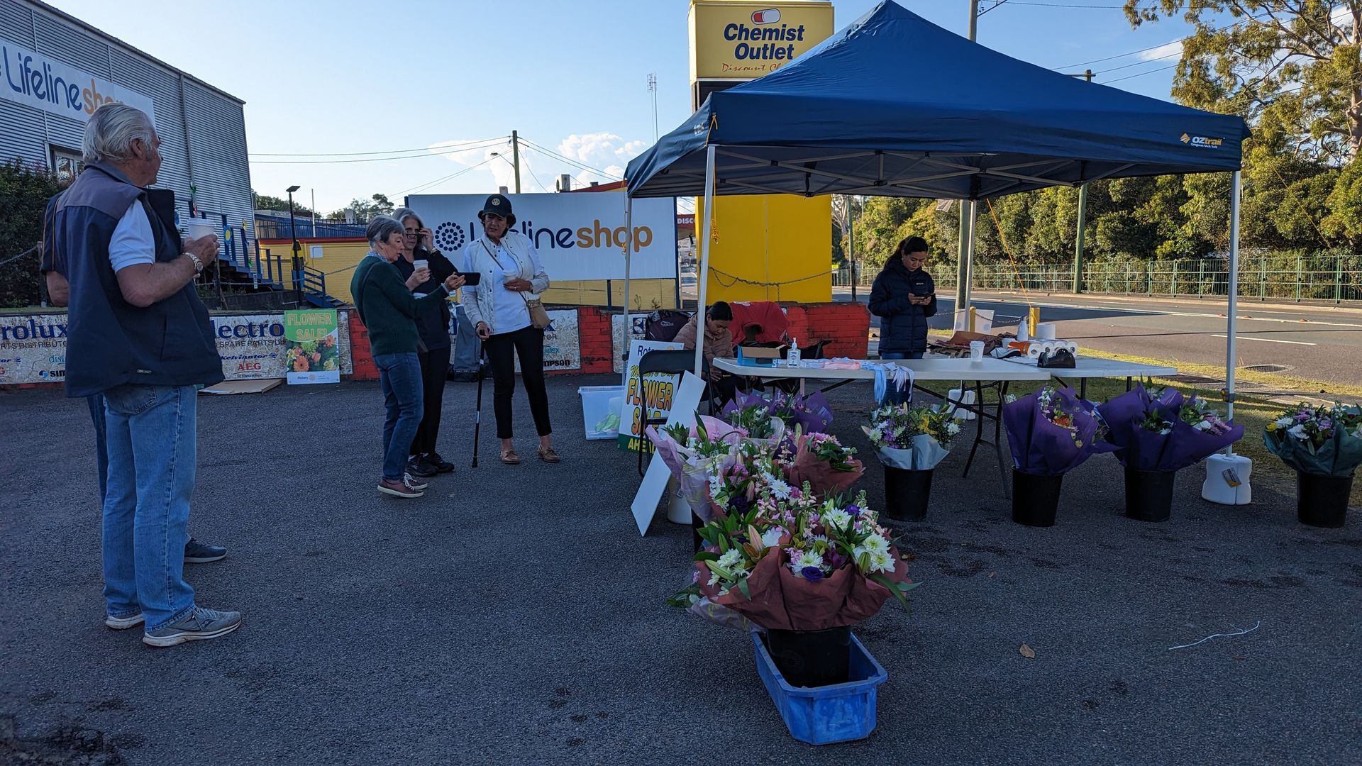 A group of people are standing around a table with flowers under a tent.