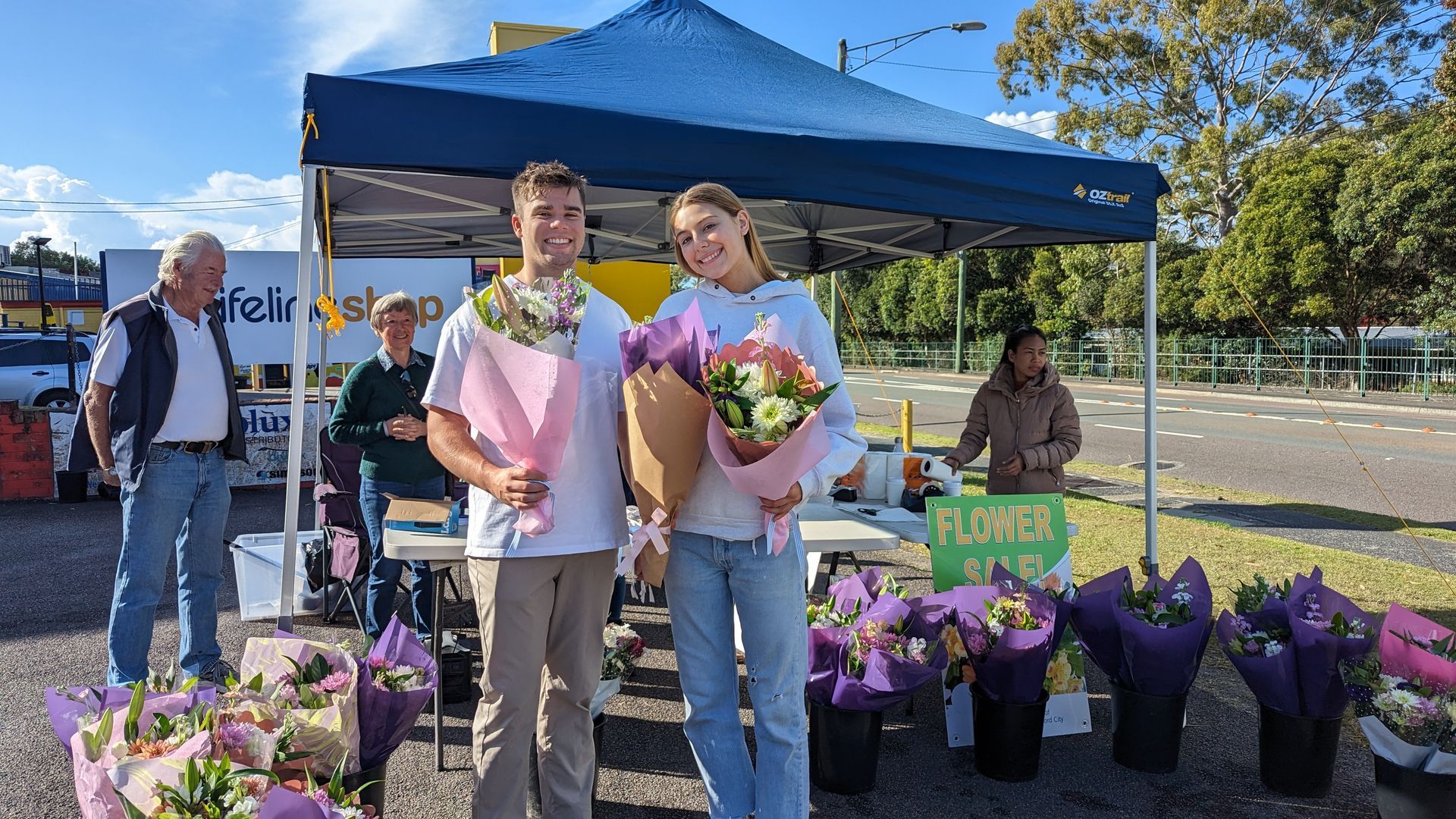 A man and a woman are standing in front of a tent holding bouquets of flowers.