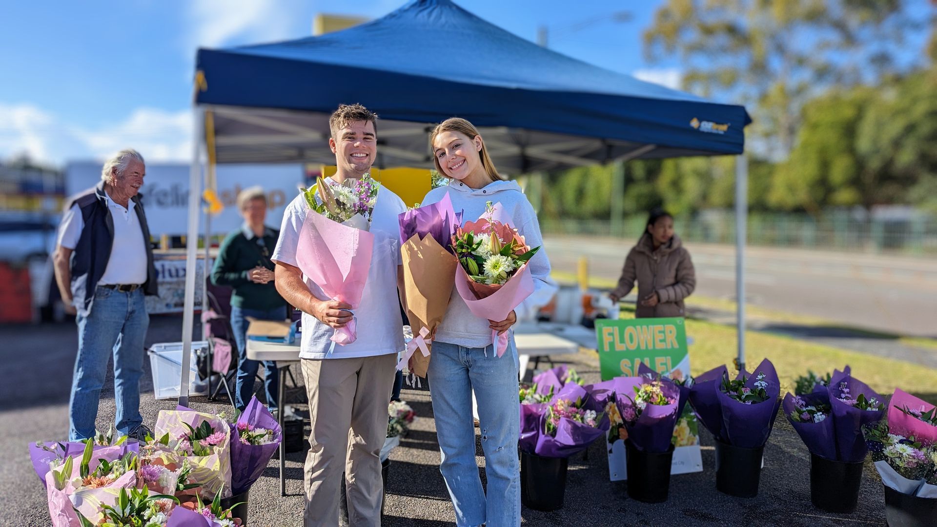 A man and a woman are standing in front of a tent holding bouquets of flowers.
