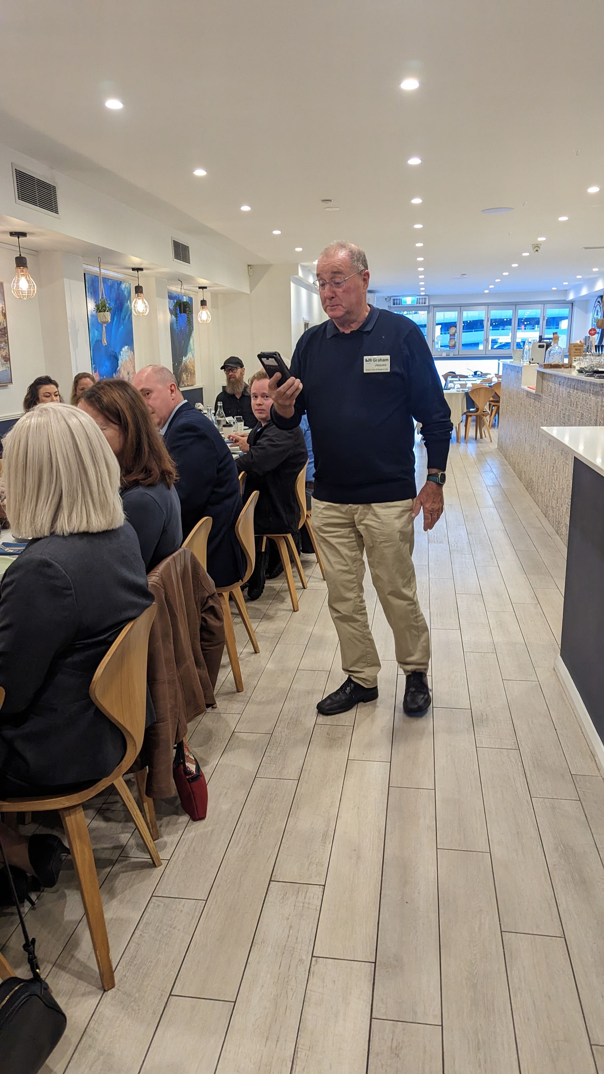 A man is standing in front of a group of people sitting at tables in a restaurant.