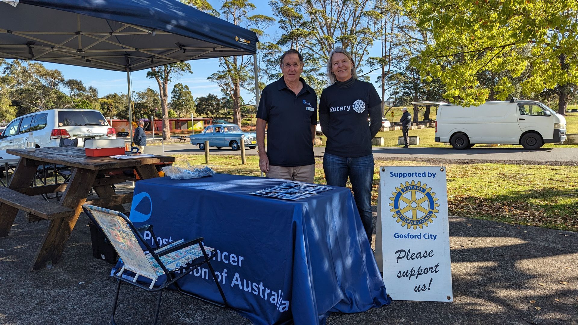 Two men are standing next to a table in a park.