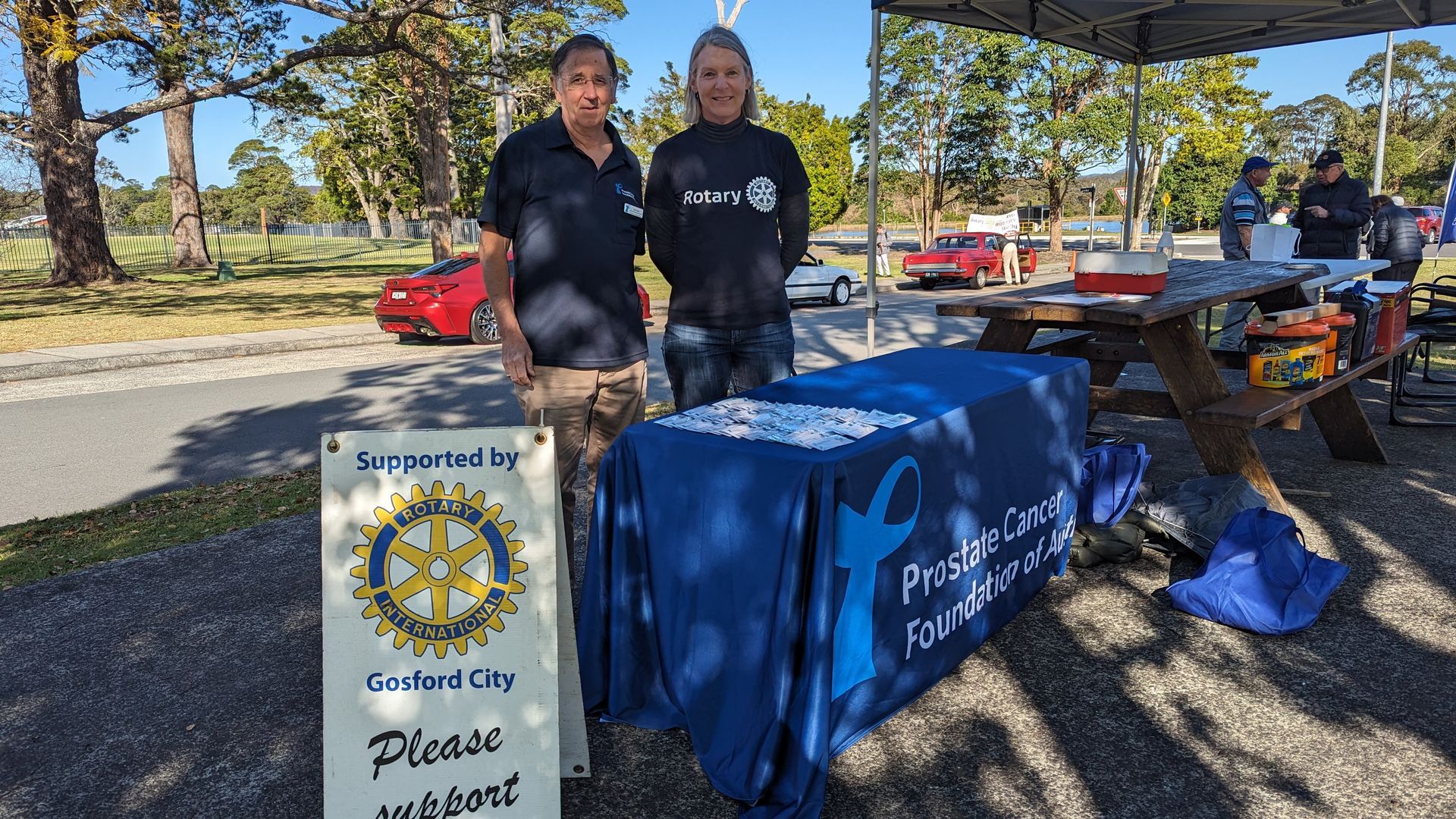 Two people are standing in front of a table with a sign that says please duck out.