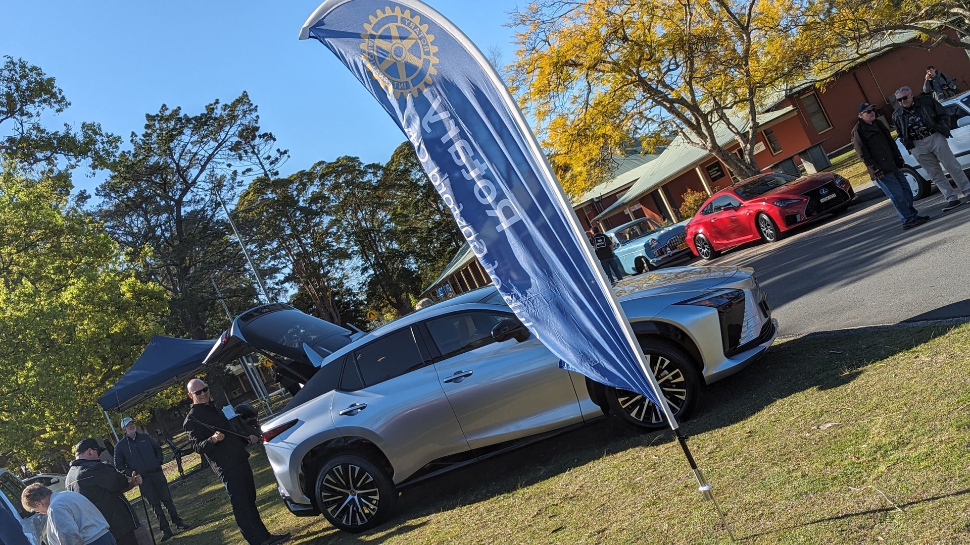 A silver car is parked in a grassy field with a blue flag hanging from it.