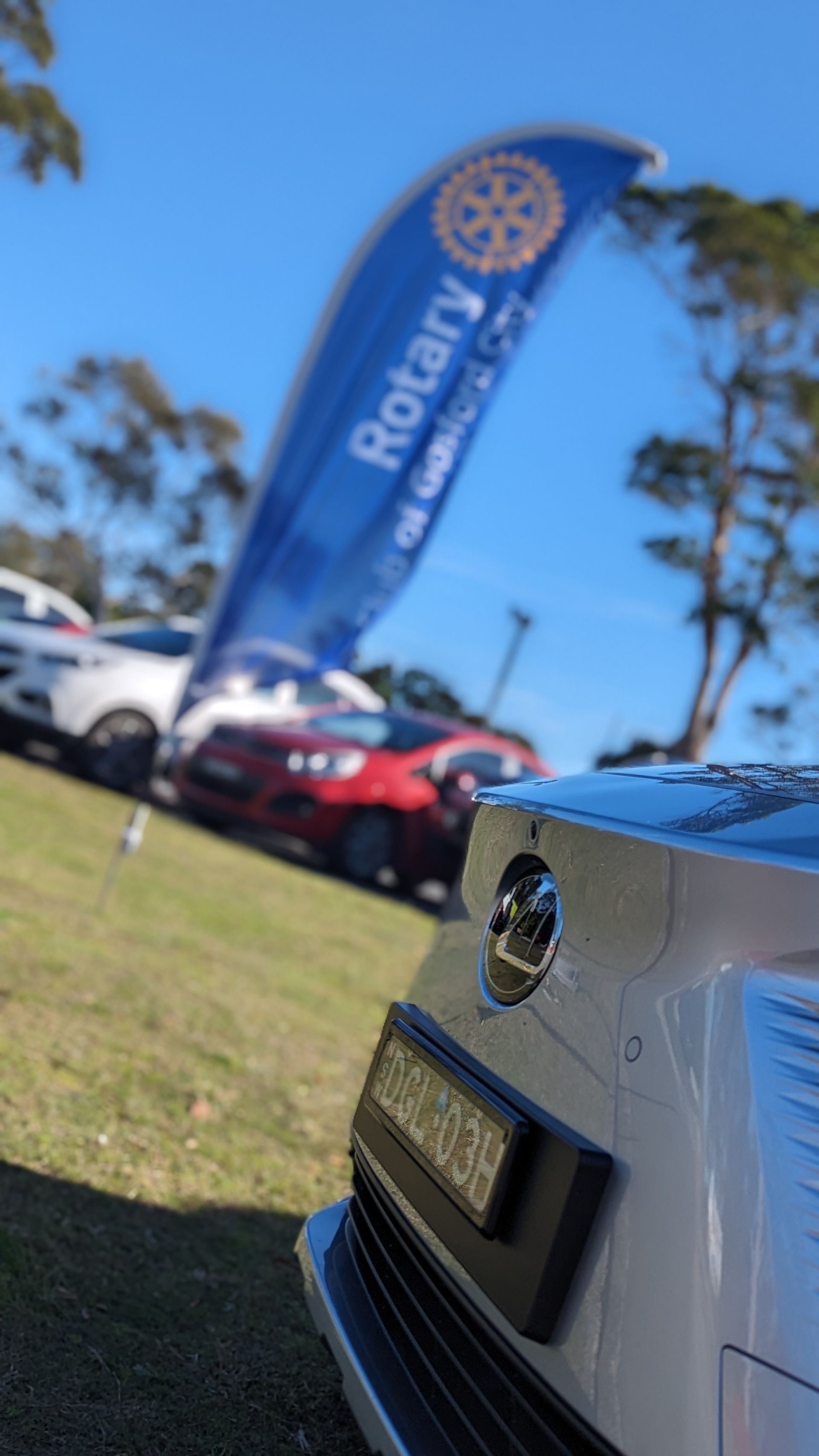 A silver car is parked in a grassy field with a rotary flag in the background.