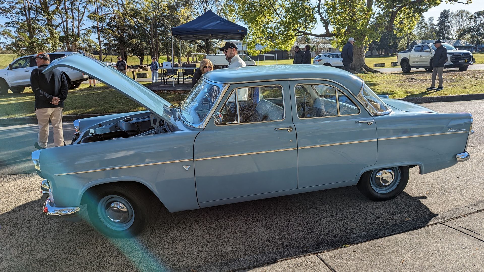 A blue car with the hood up is parked on the side of the road.