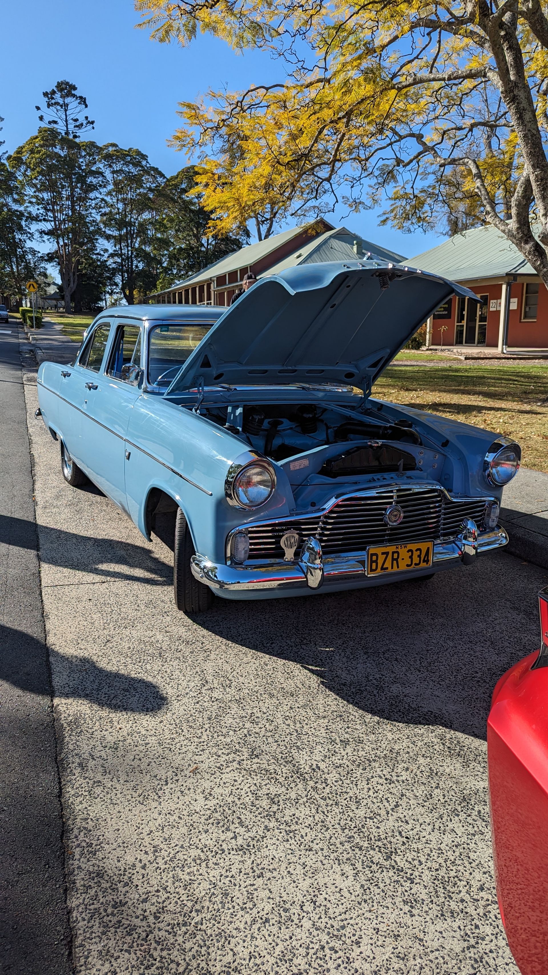 A blue car with the hood up is parked on the side of the road.