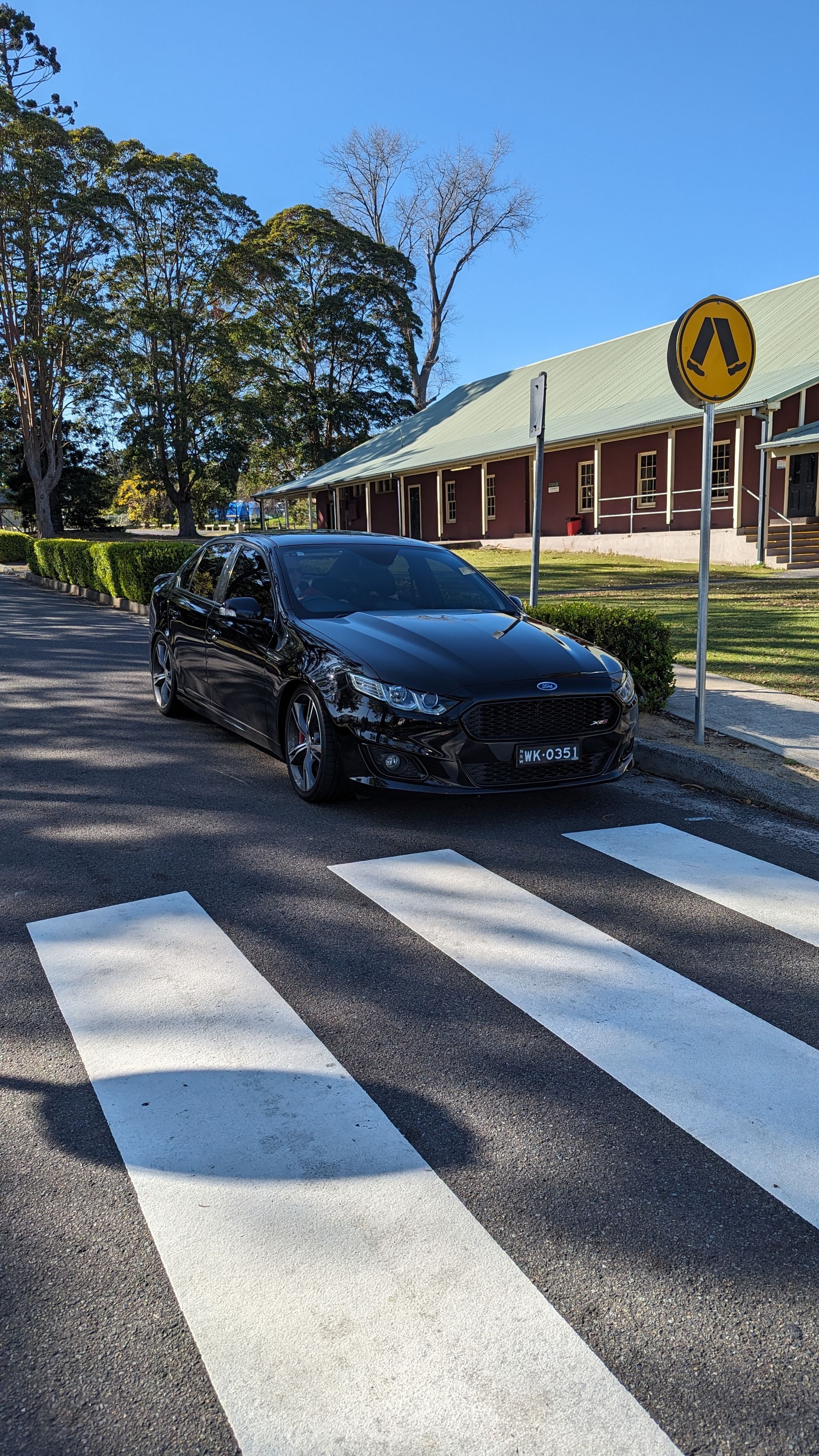 A black car is parked on the side of the road at a crosswalk.