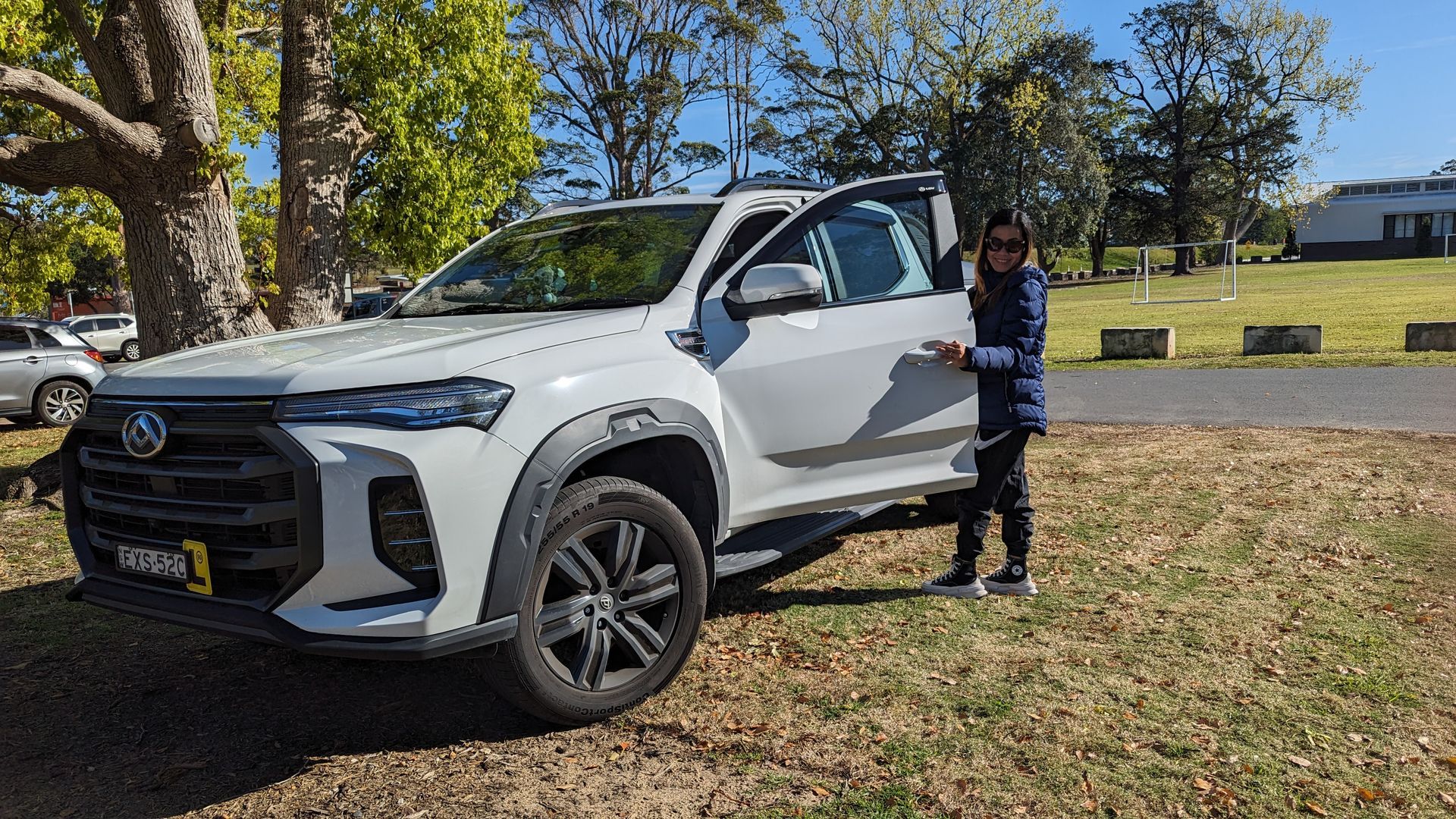A woman is standing next to a white truck in a field.