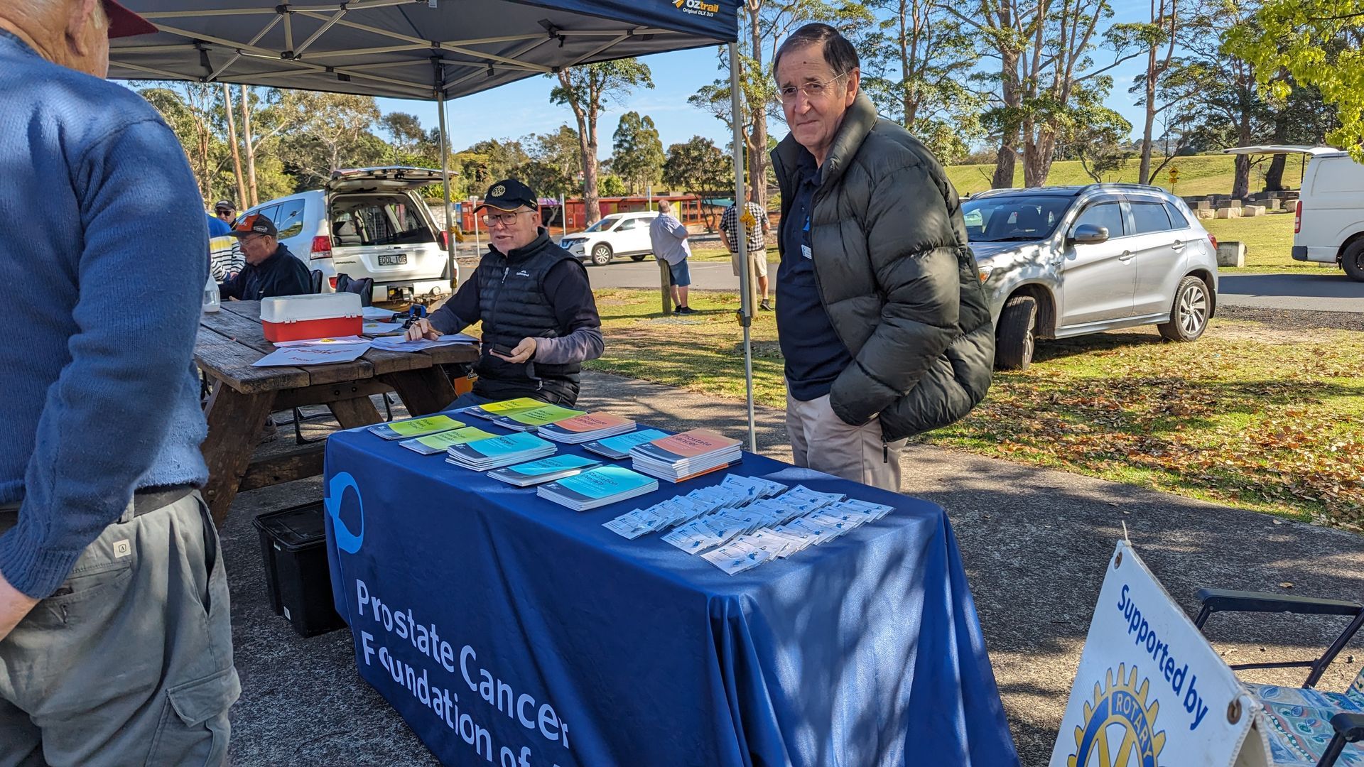 A group of people are standing around a table in a park.
