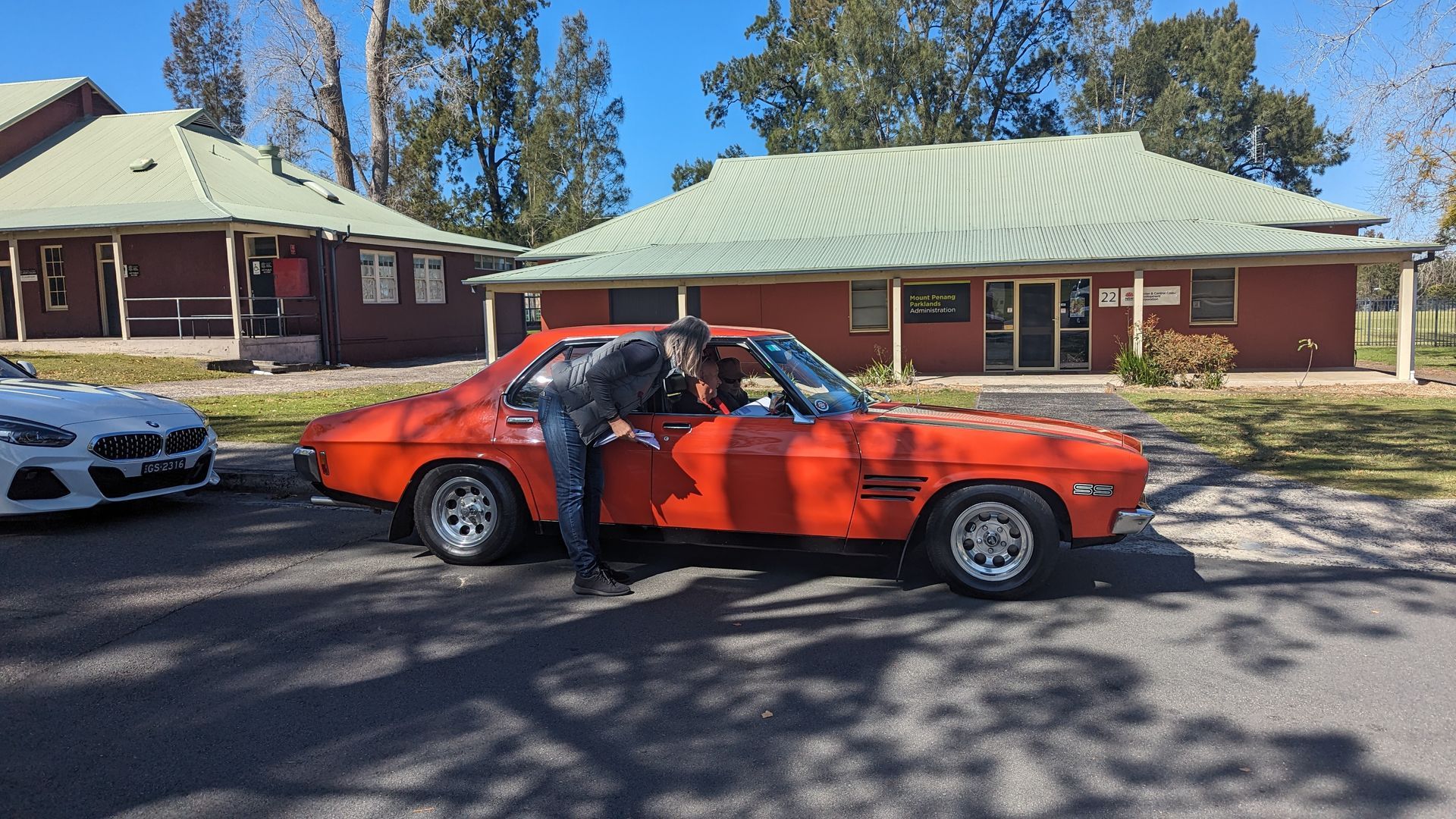 A man is standing next to a red car in front of a house.