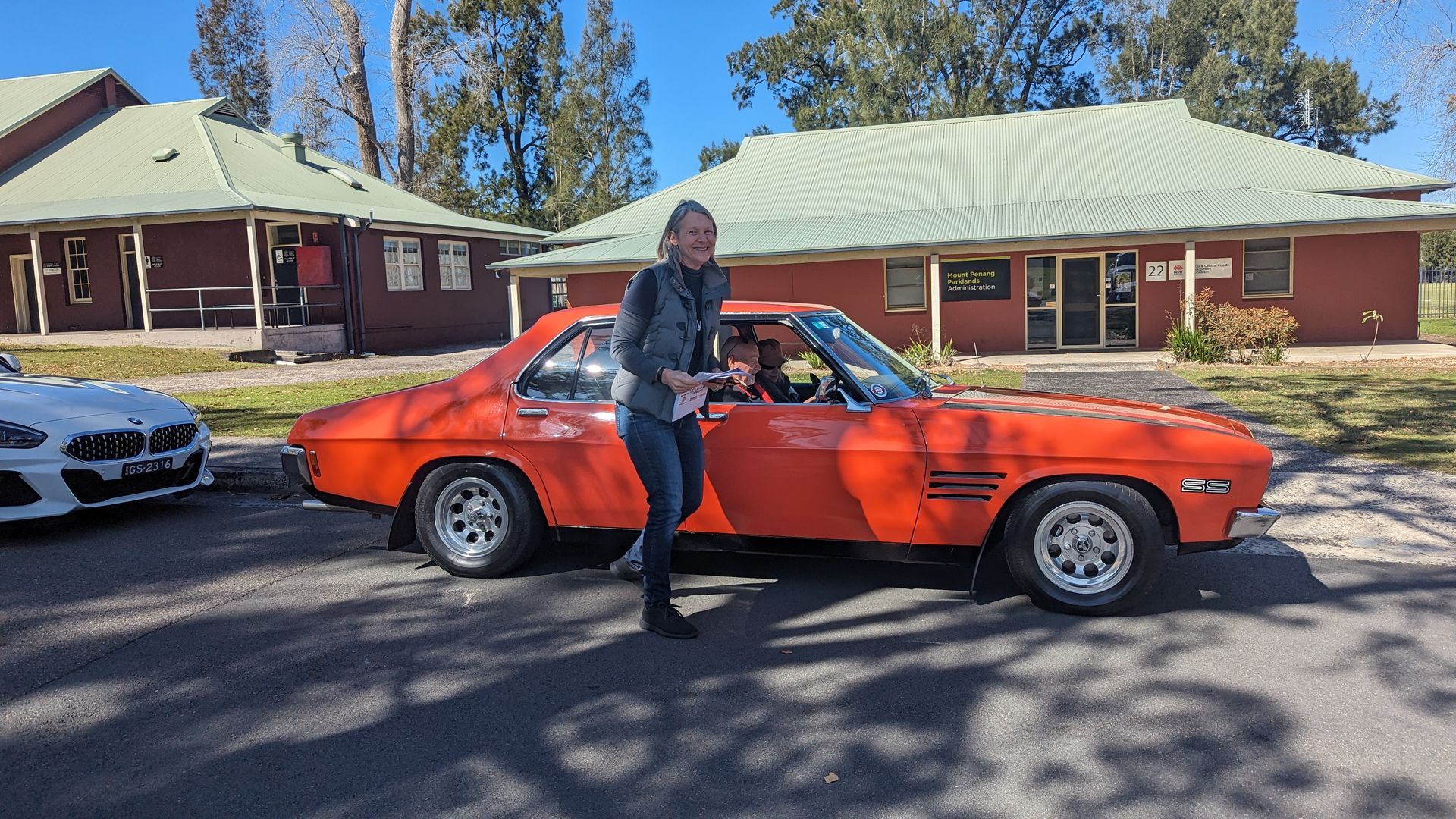 A man is standing next to an orange car in front of a house.