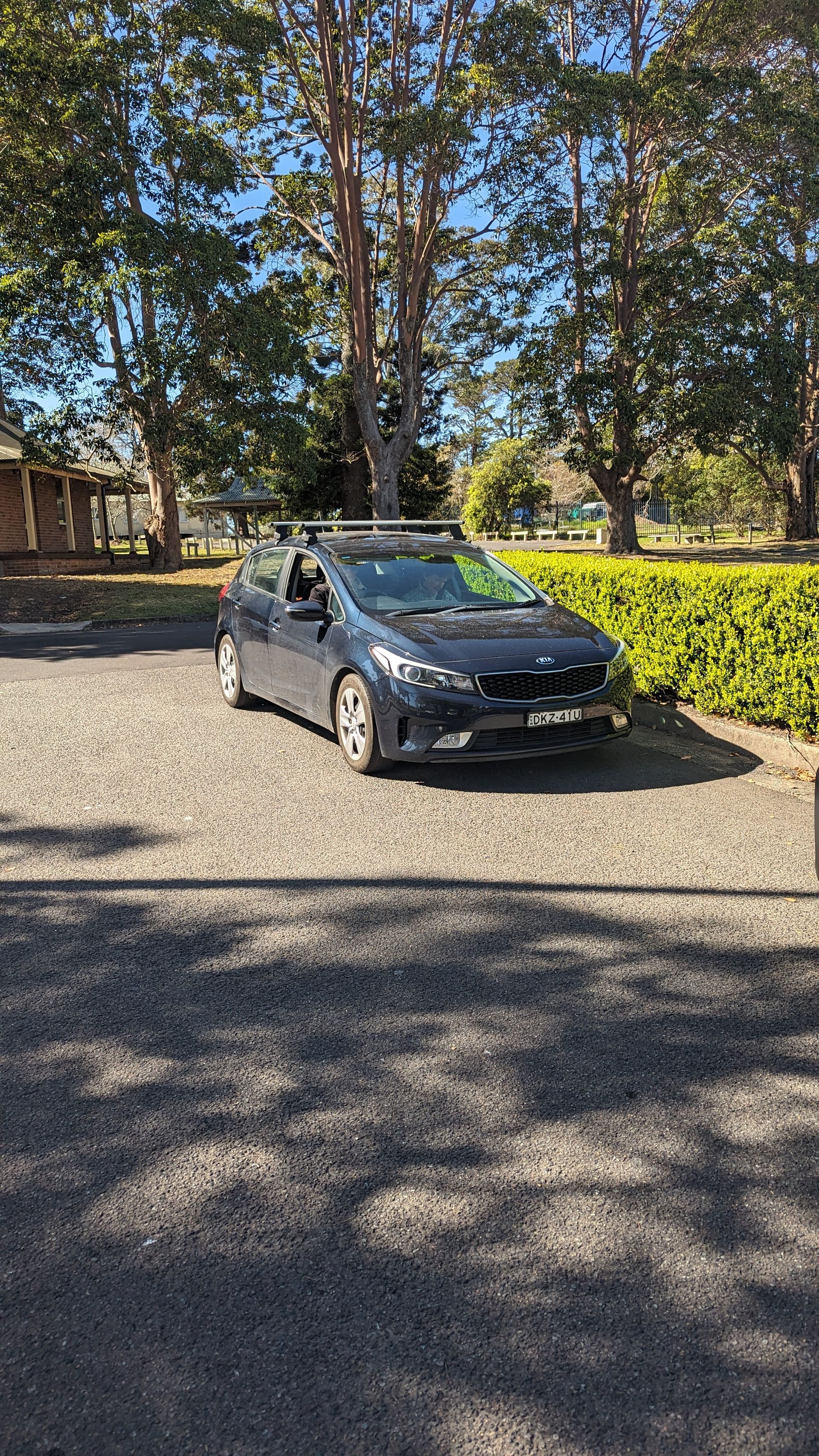 A black car is parked in a gravel driveway surrounded by trees.