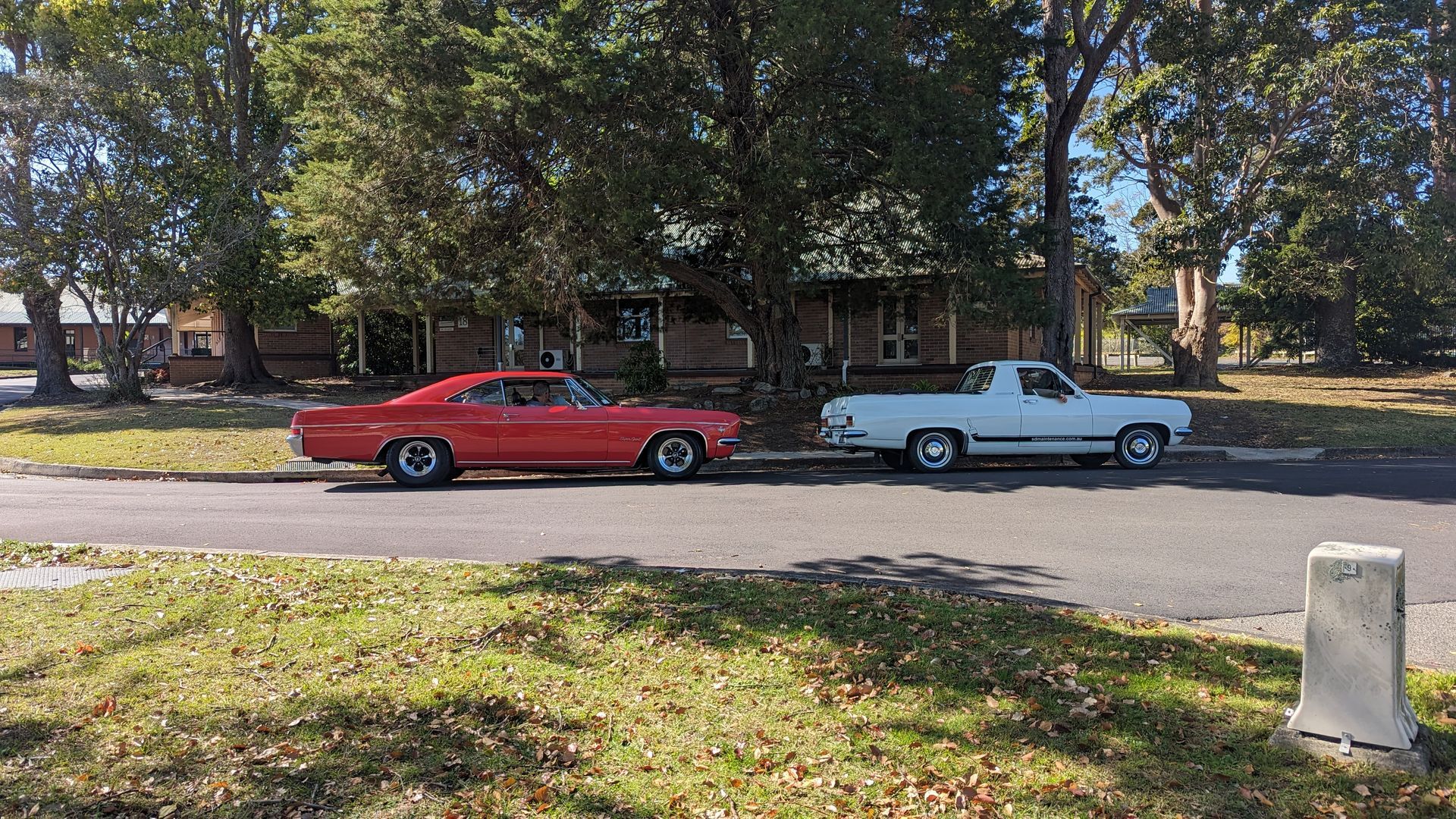 A red car and a white truck are parked on the side of the road.