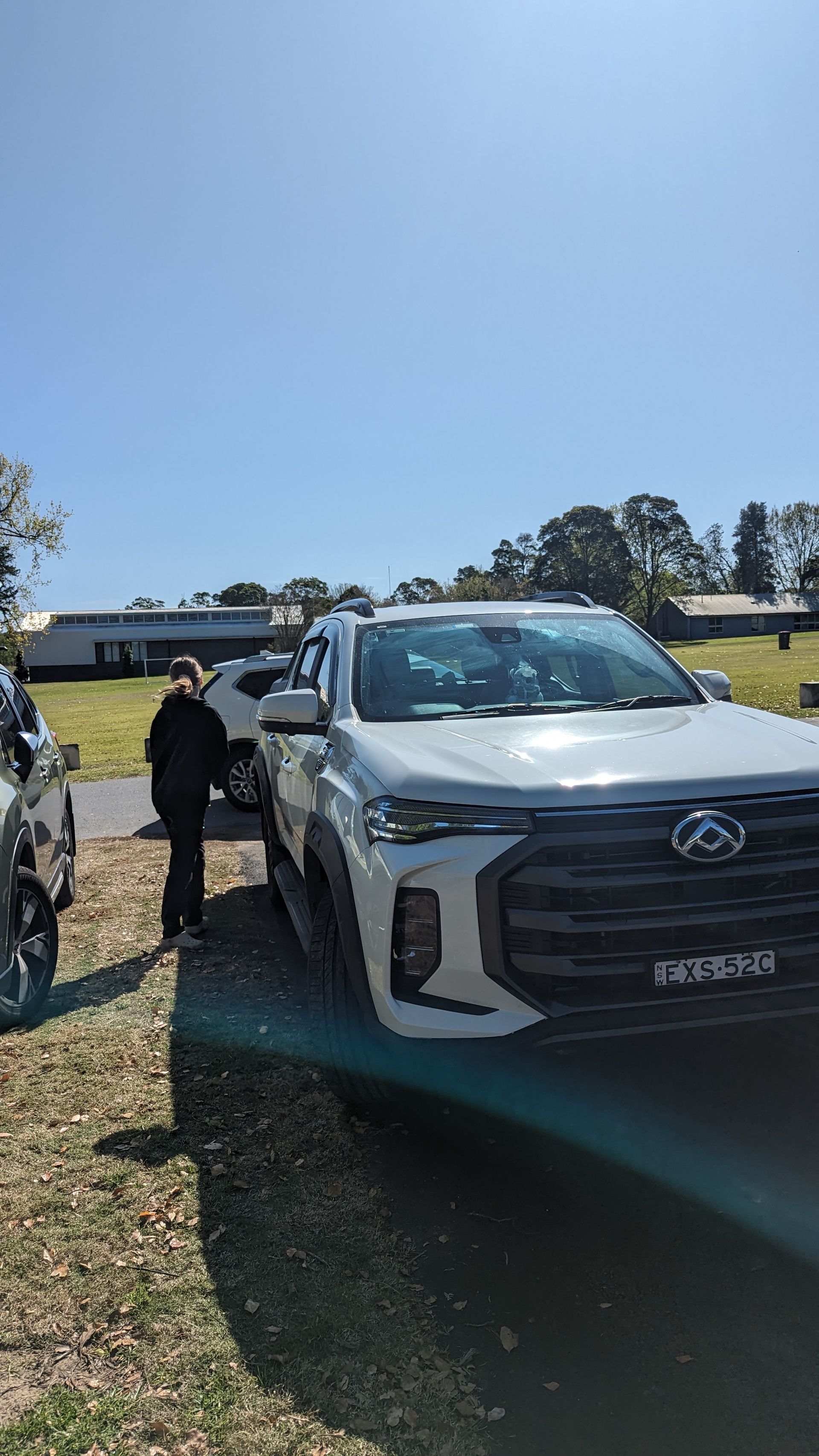 A man is standing next to a white suv parked in a grassy field.