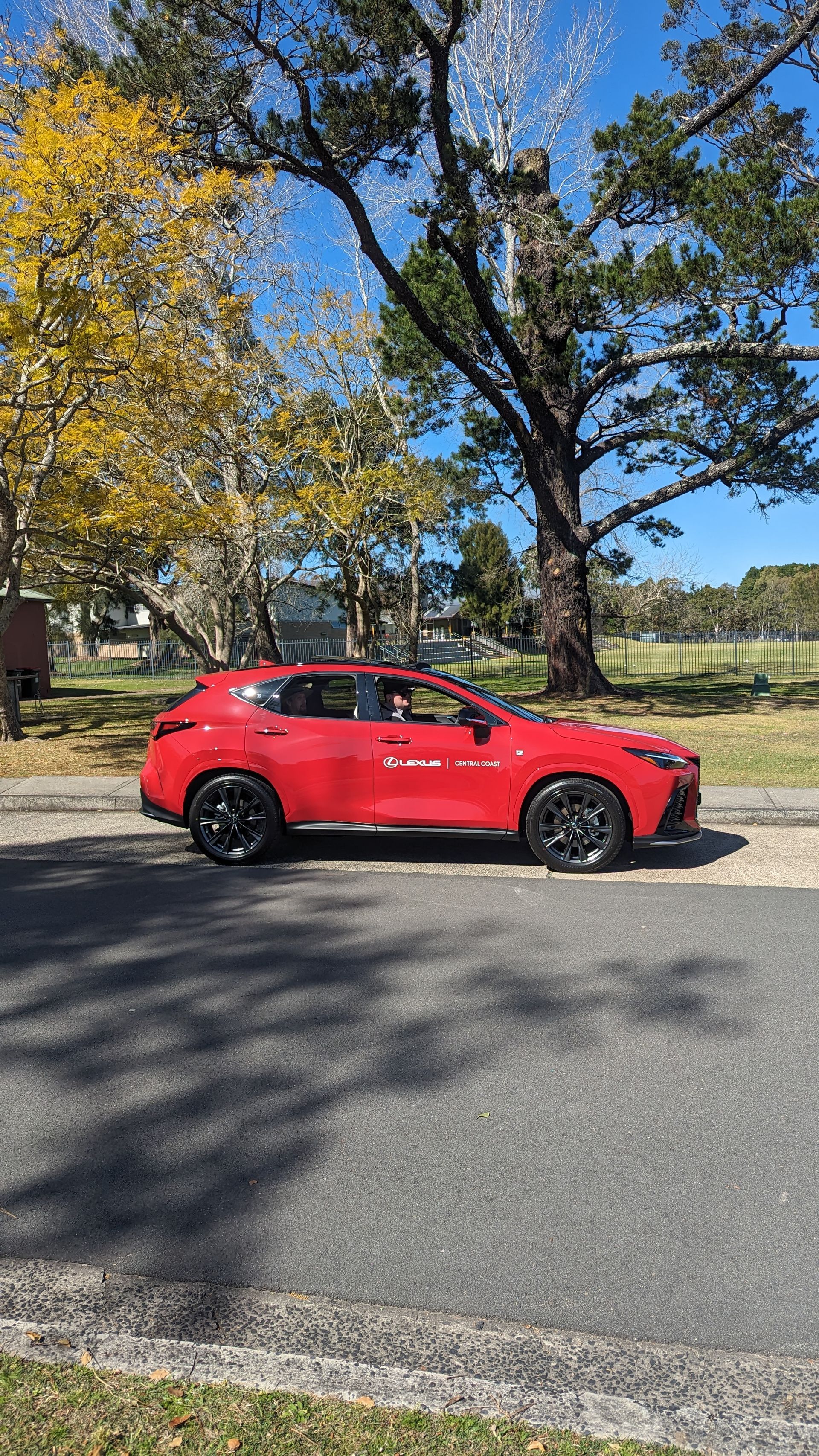 A red car is parked on the side of the road next to a tree.