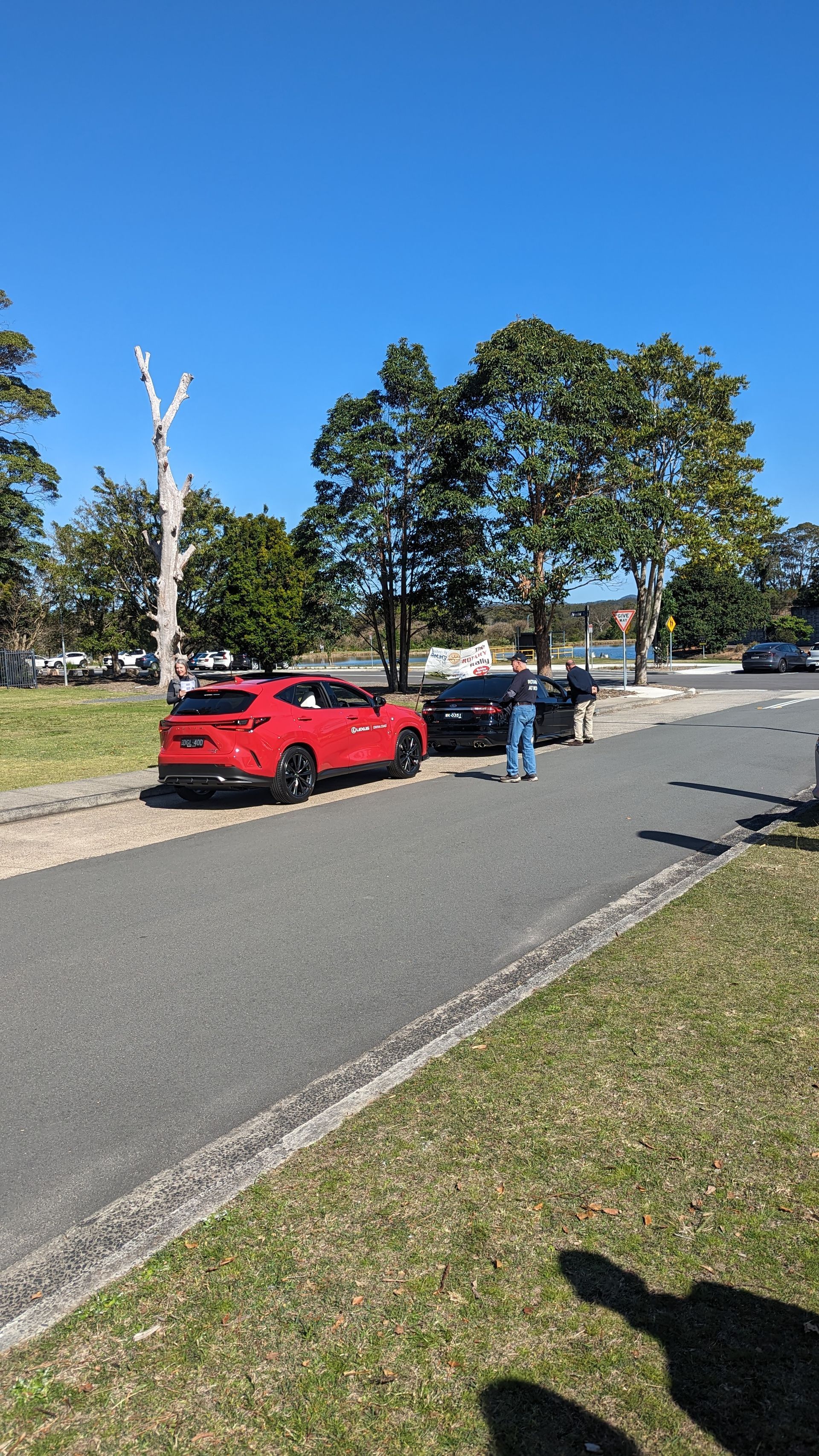 A red car is parked on the side of the road next to a tree.
