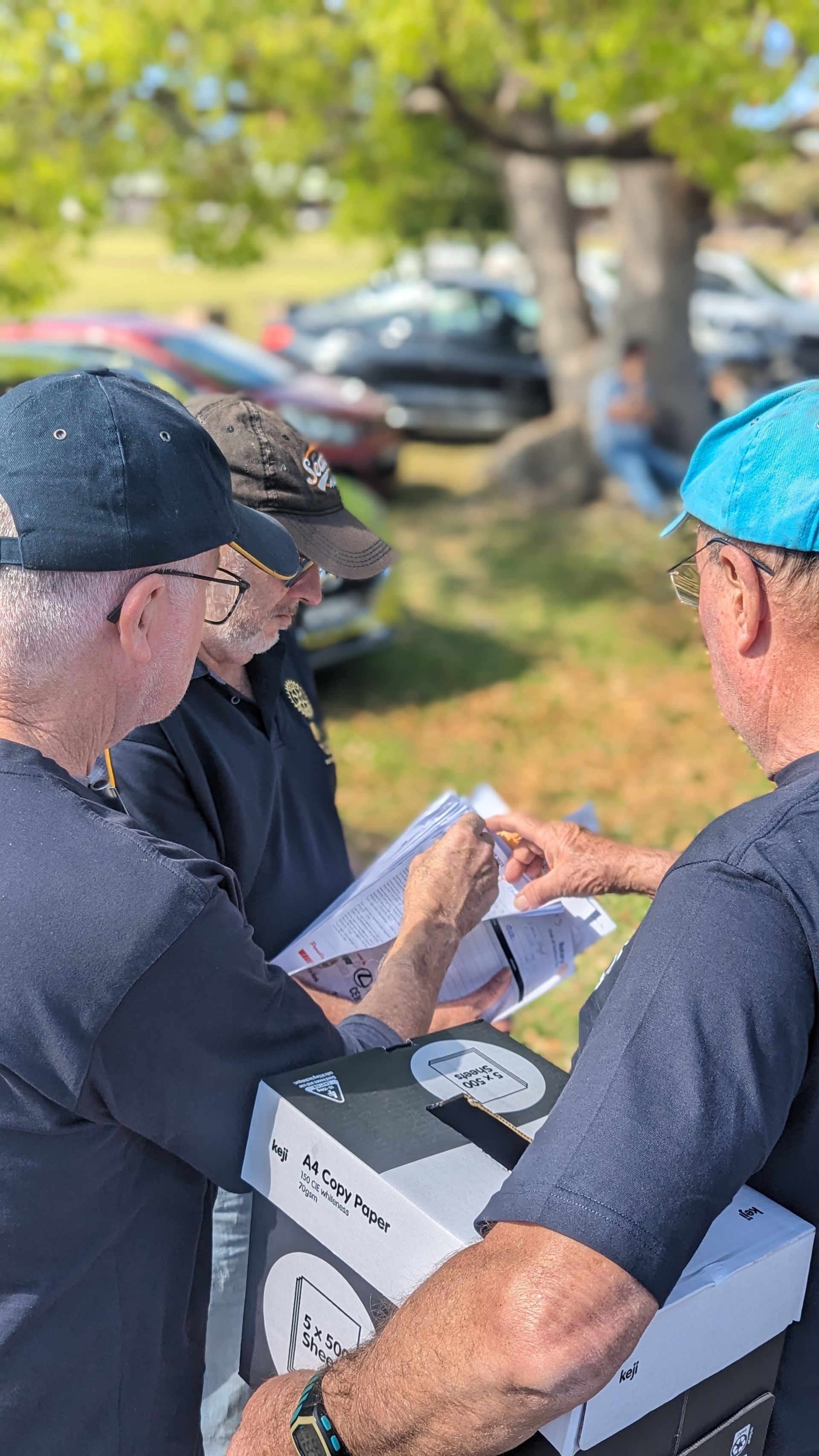 A group of men are standing in a park looking at papers.