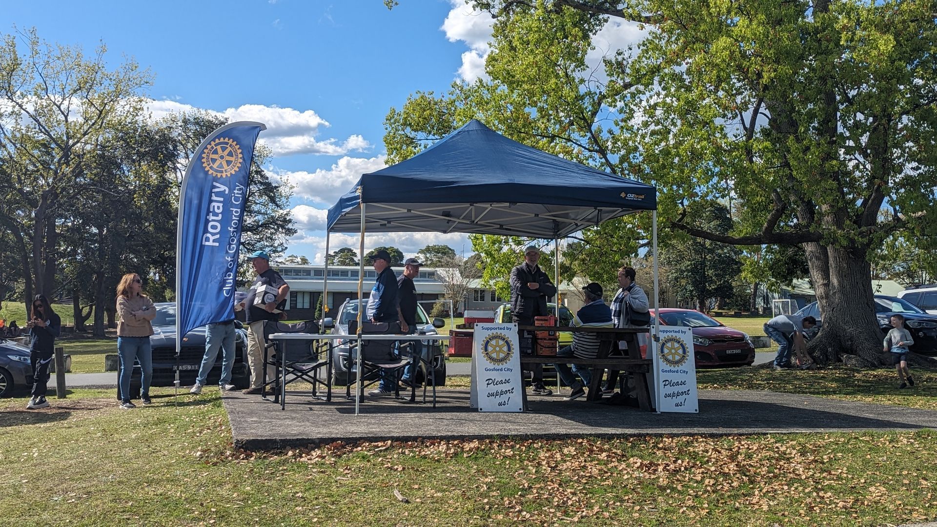 A group of people are standing under a tent in a park.