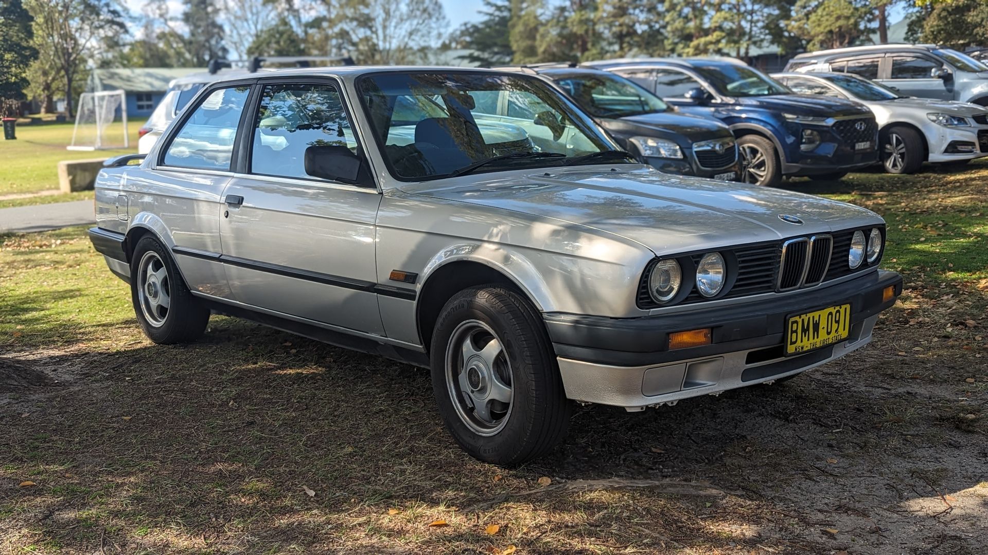 A silver bmw e30 is parked in a parking lot.