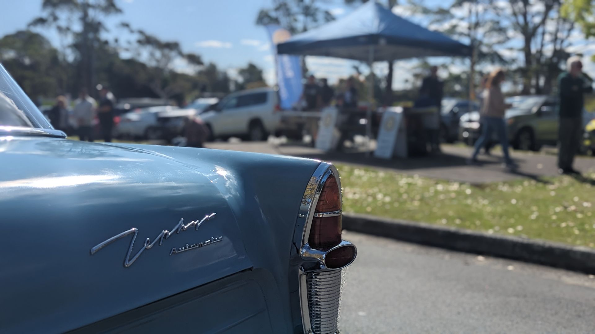 A blue car is parked on the side of the road at a car show.