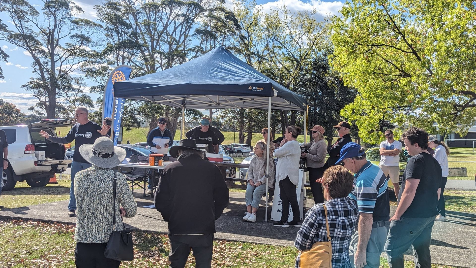A group of people are standing around a tent in a park.