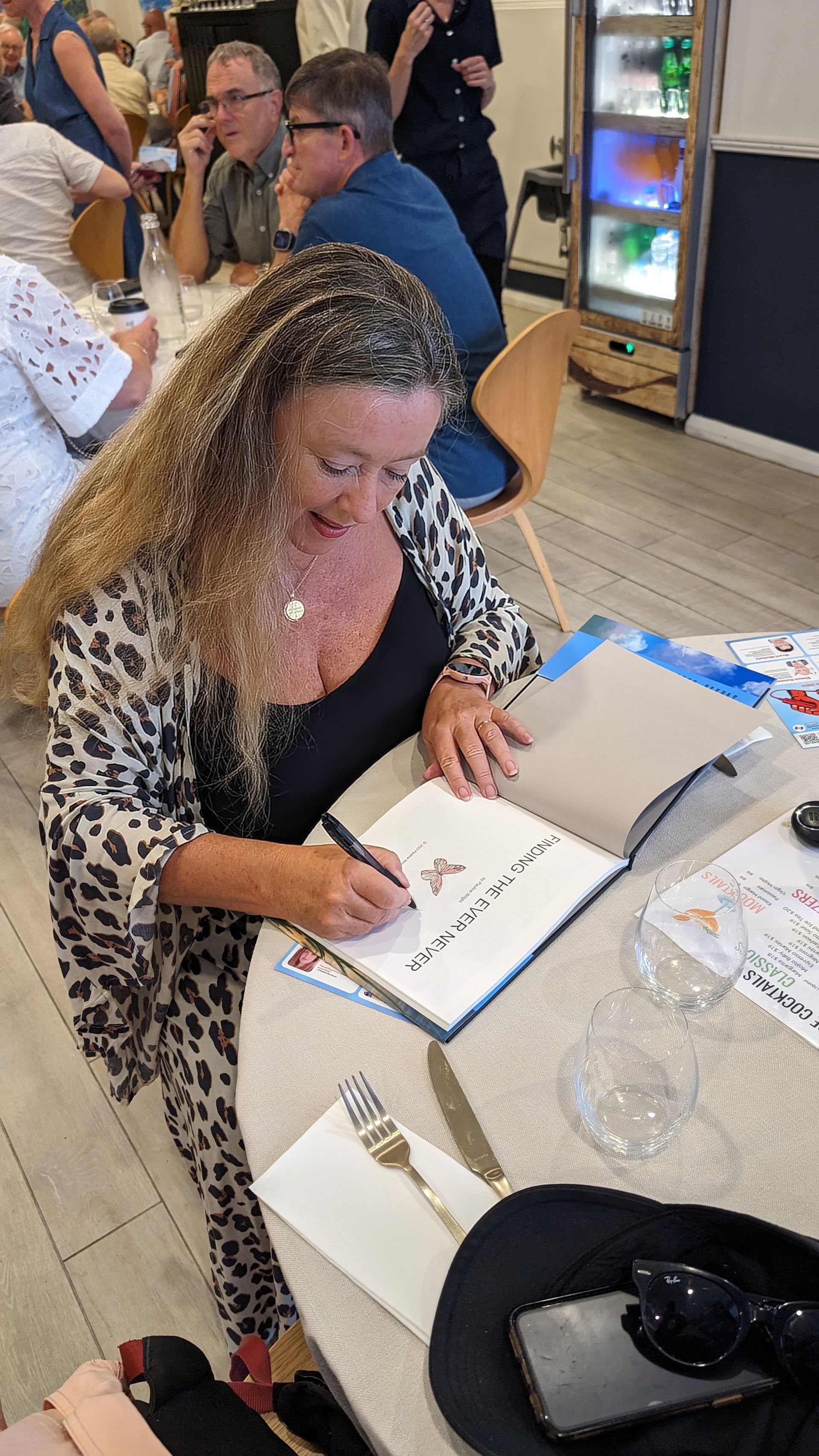A woman is sitting at a table signing a book.
