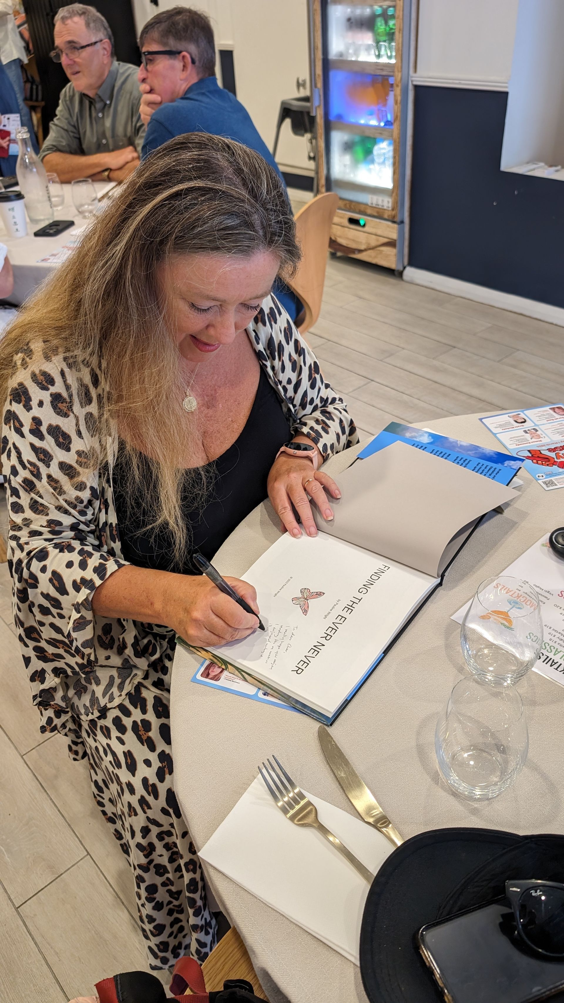 A woman is sitting at a table signing a book.