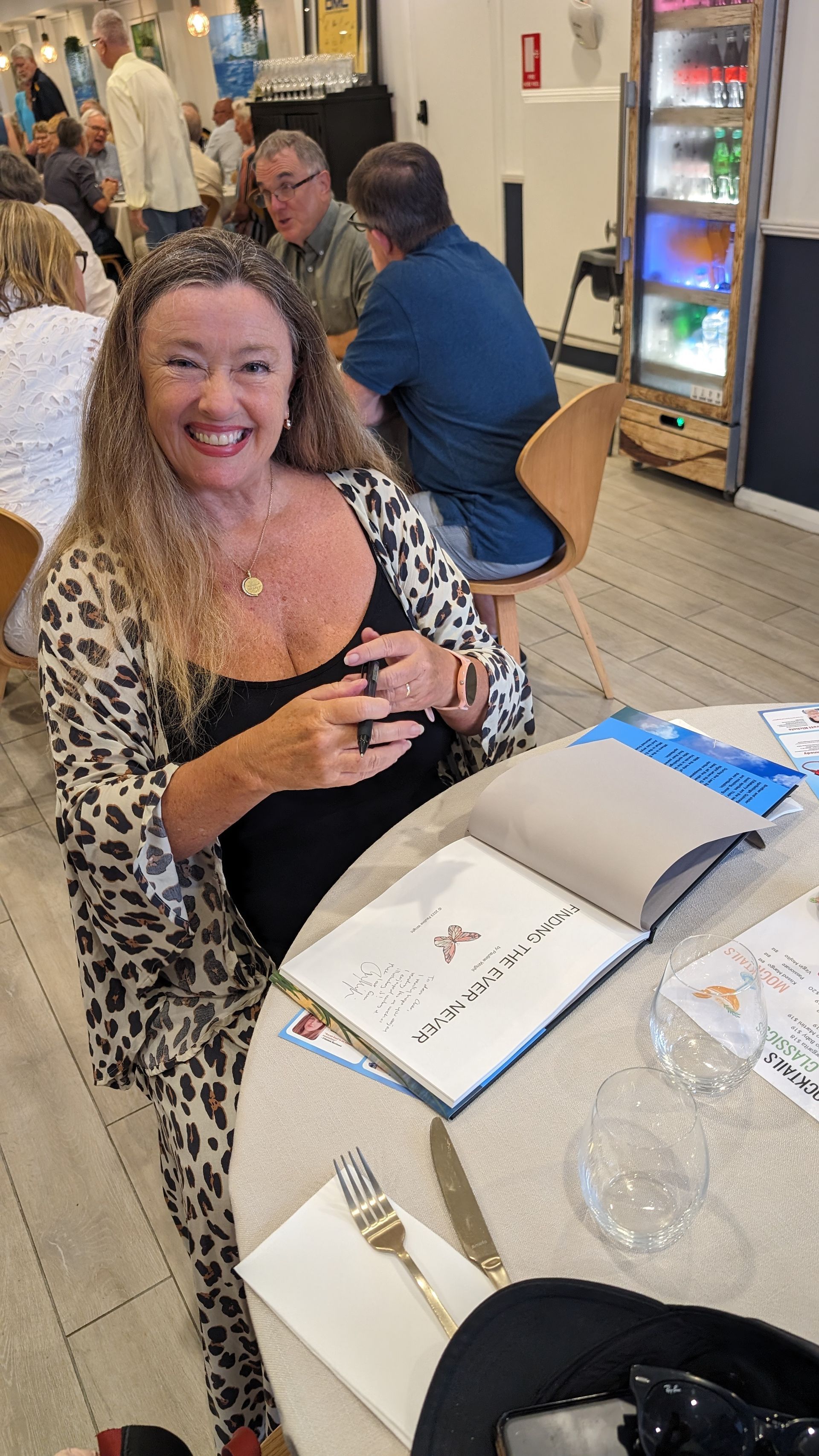 A woman is smiling while sitting at a table in a restaurant.