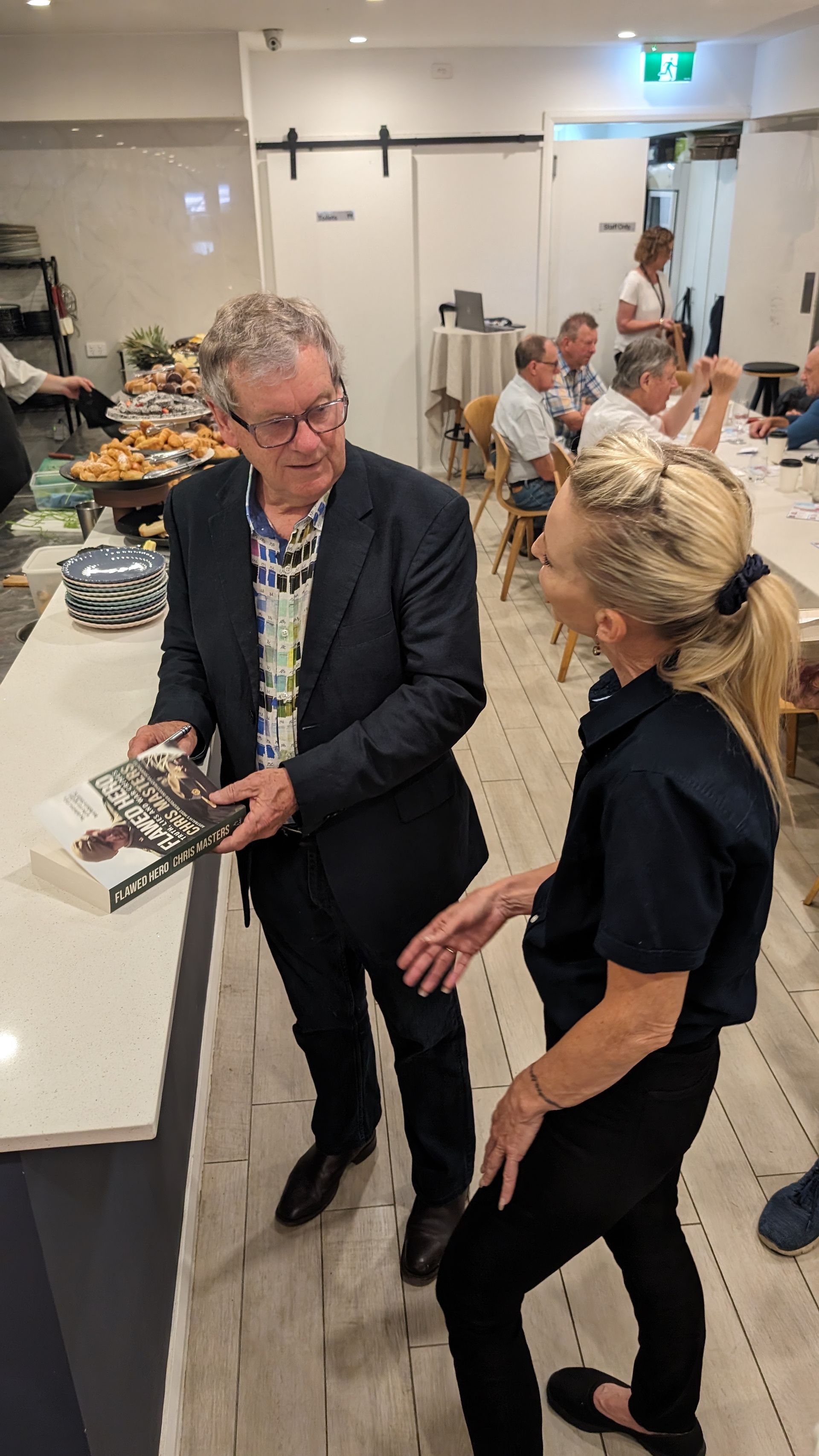 A man and a woman are standing next to each other in a room . the man is holding a book.