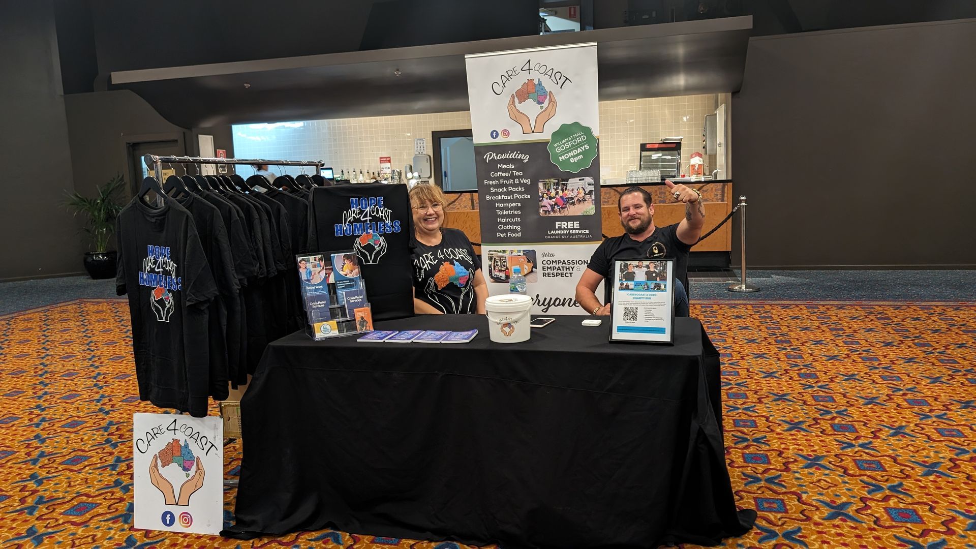 Two men are sitting at a table in front of a display of shirts.