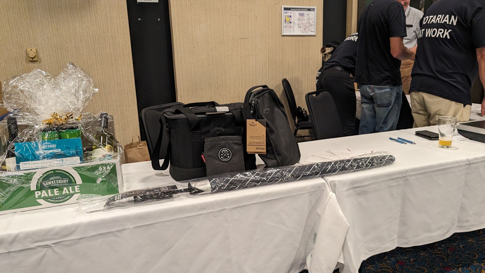 A group of people are standing around a table with a bag on it.