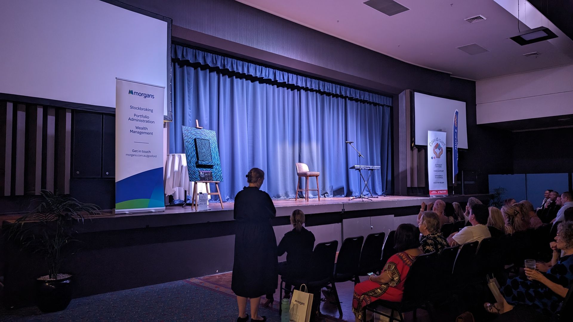 A group of people are sitting in an auditorium watching a presentation on a stage.