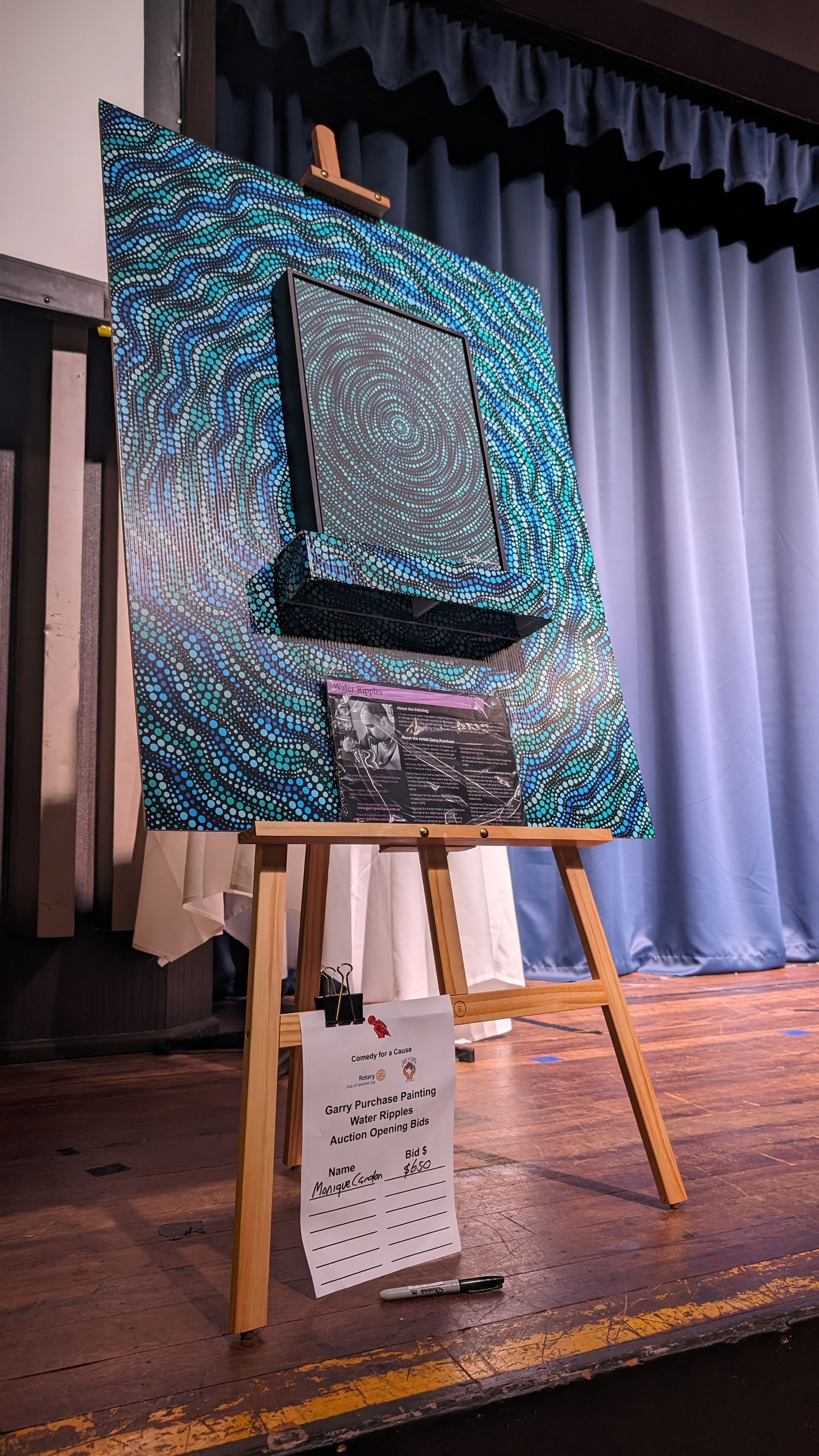 A large painting is sitting on a wooden easel on a stage.