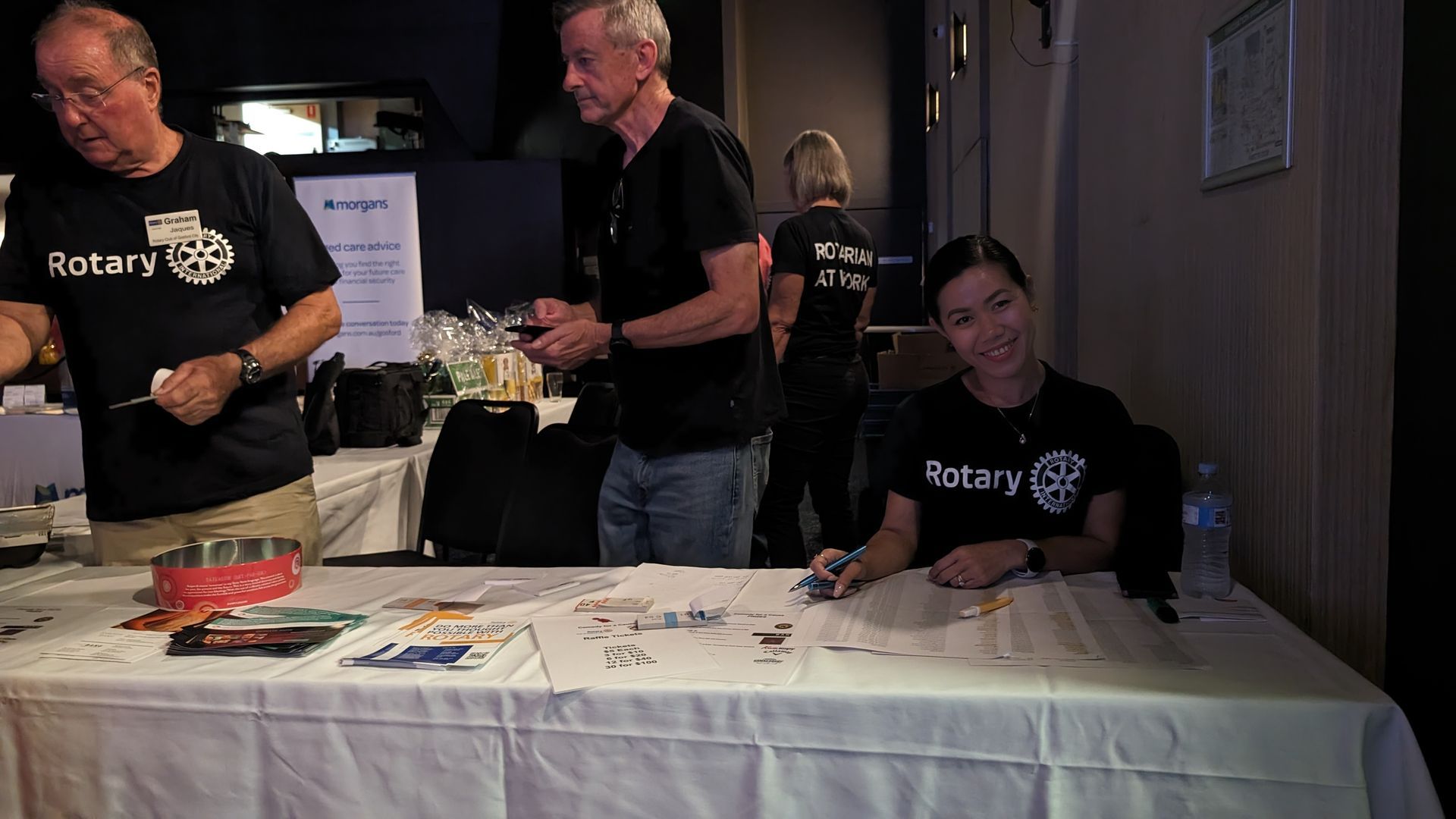 A group of people standing around a table with a woman sitting at it.