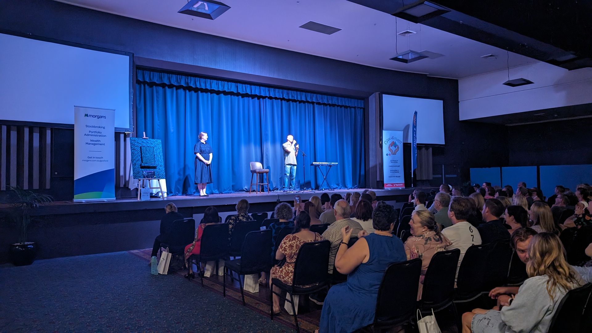 A group of people are sitting in front of a stage in a large auditorium.