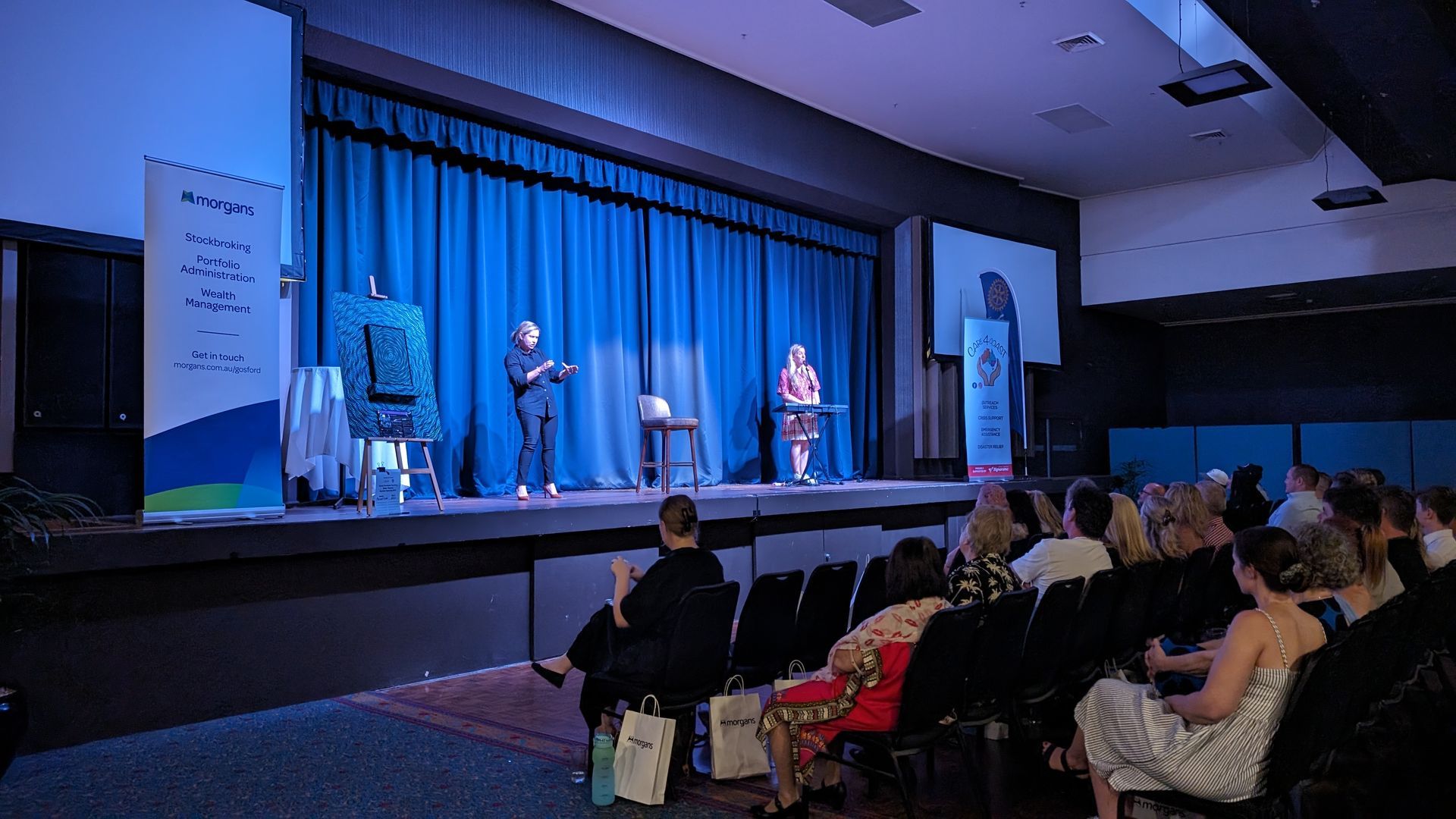 A group of people are sitting in front of a stage in a large auditorium.