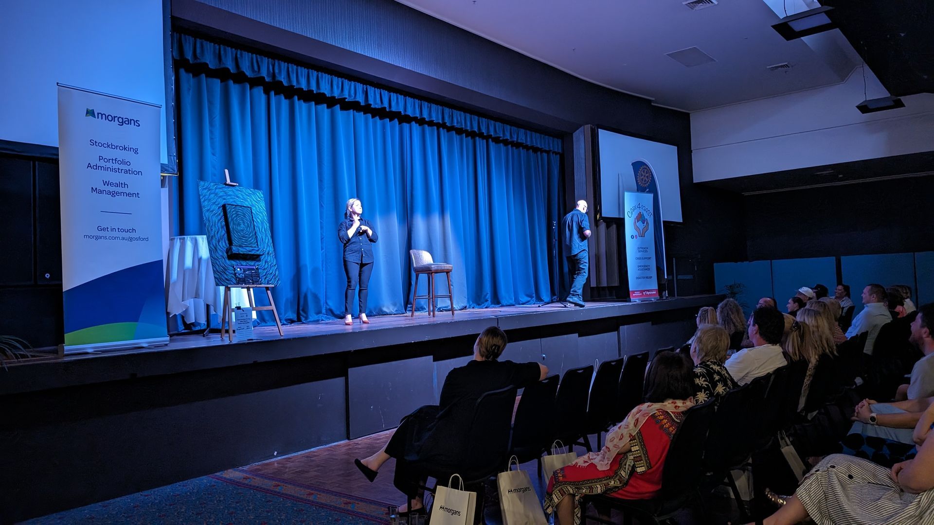 A group of people are sitting in an auditorium watching a comedy show on a stage.