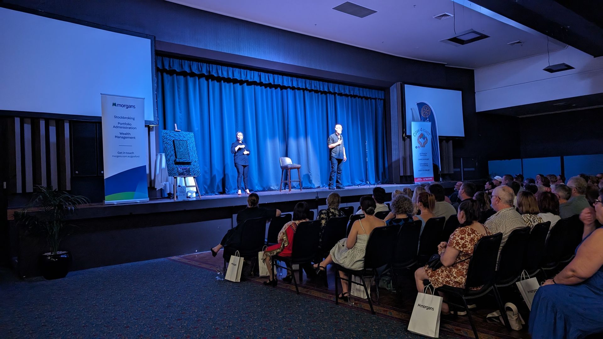 A group of people are sitting in an auditorium watching a presentation on a stage.