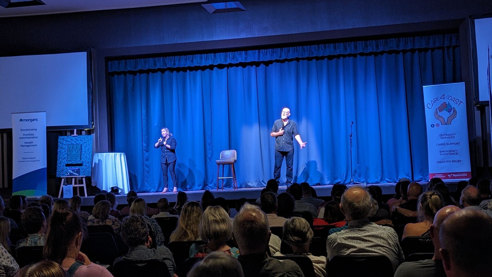 Two men are standing on a stage in front of a crowd.