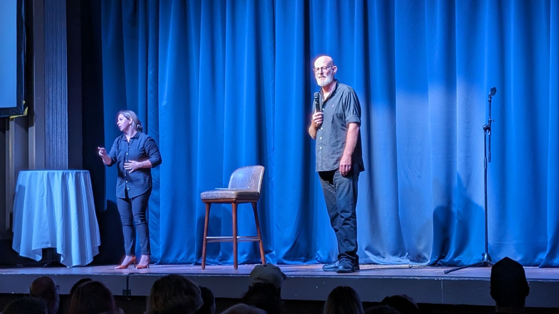 A man and a woman are standing on a stage in front of a blue curtain.