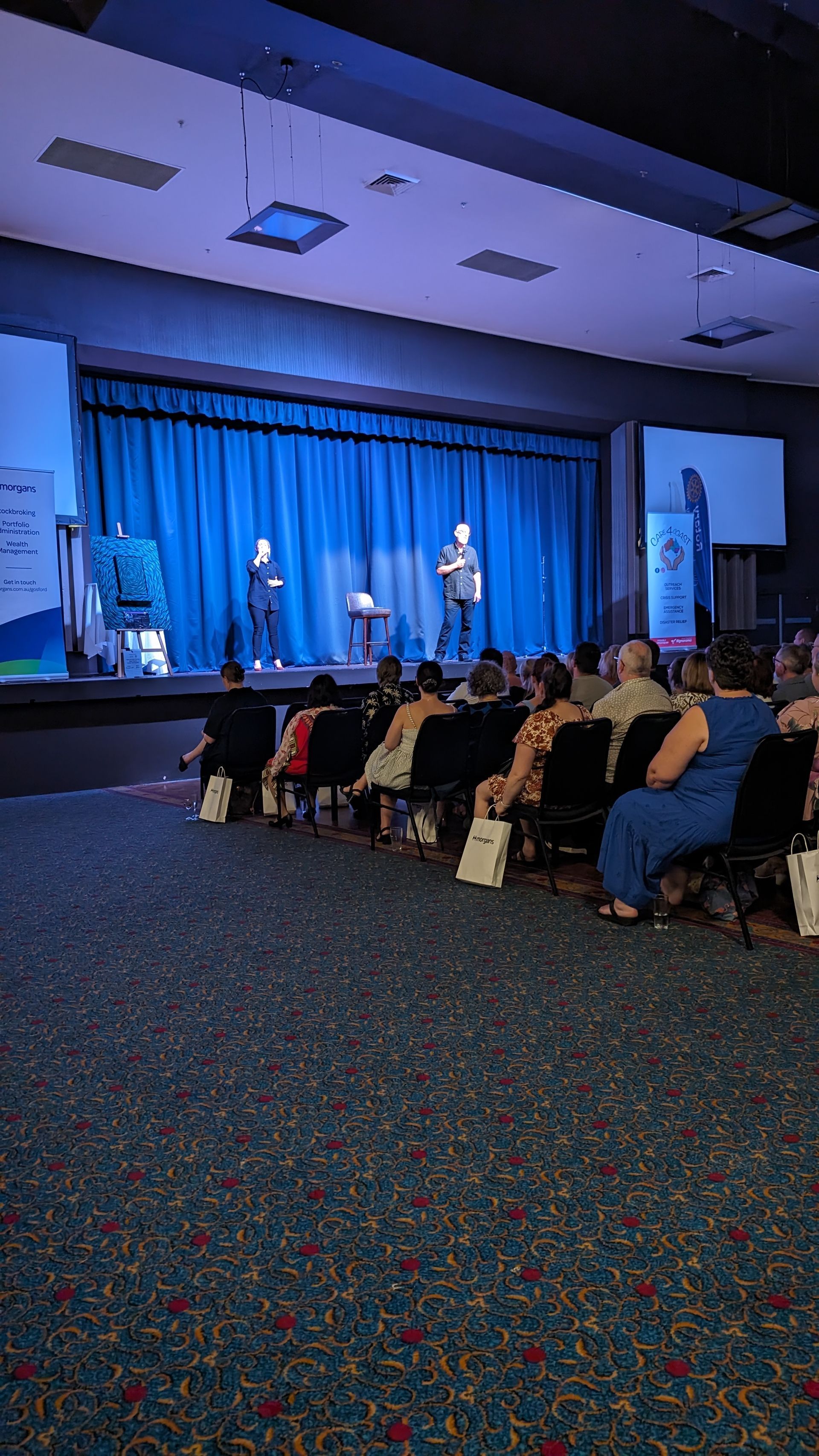 A group of people are sitting in chairs in front of a stage in a large auditorium.