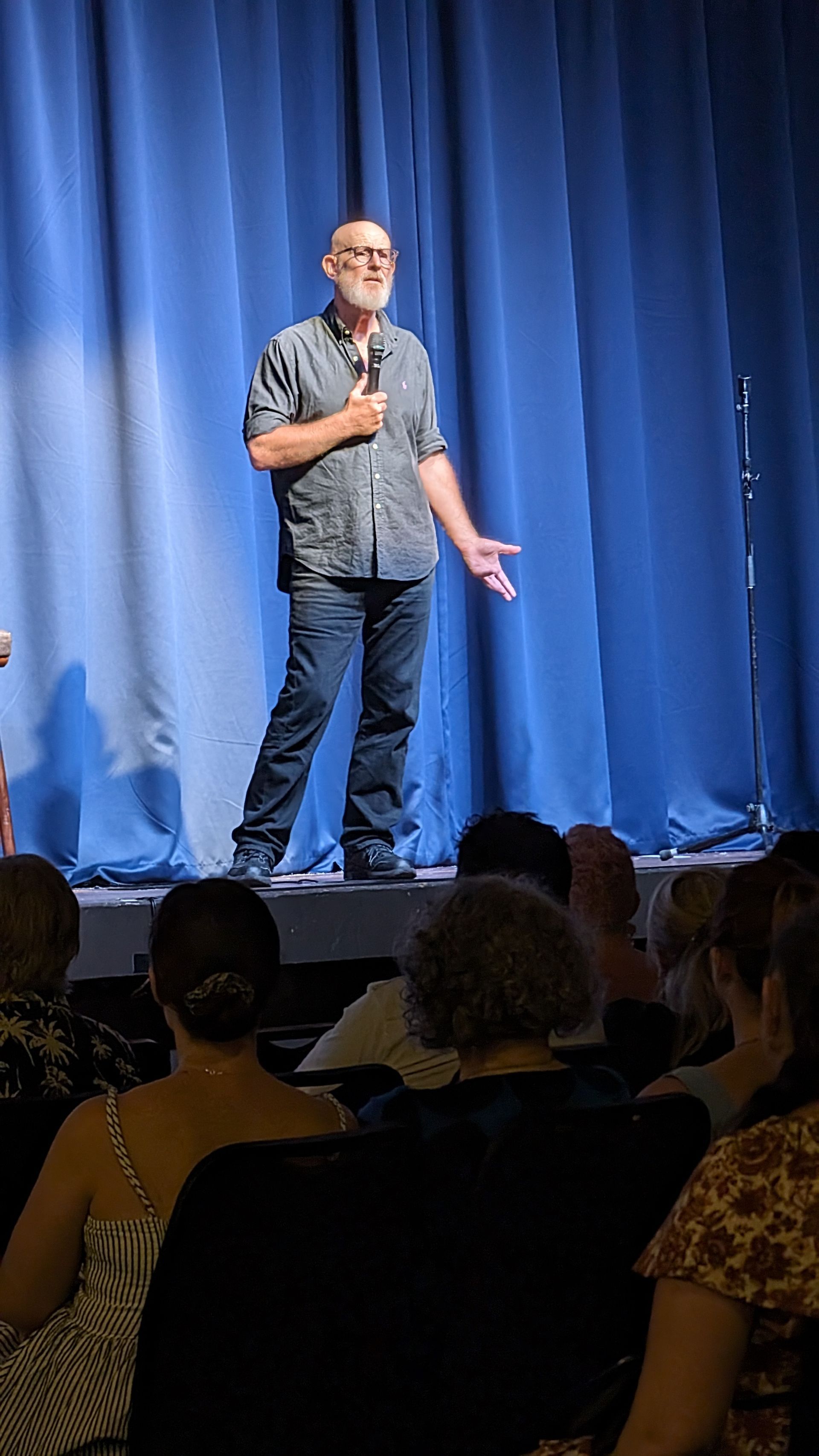 A man is standing on a stage holding a microphone in front of a crowd.