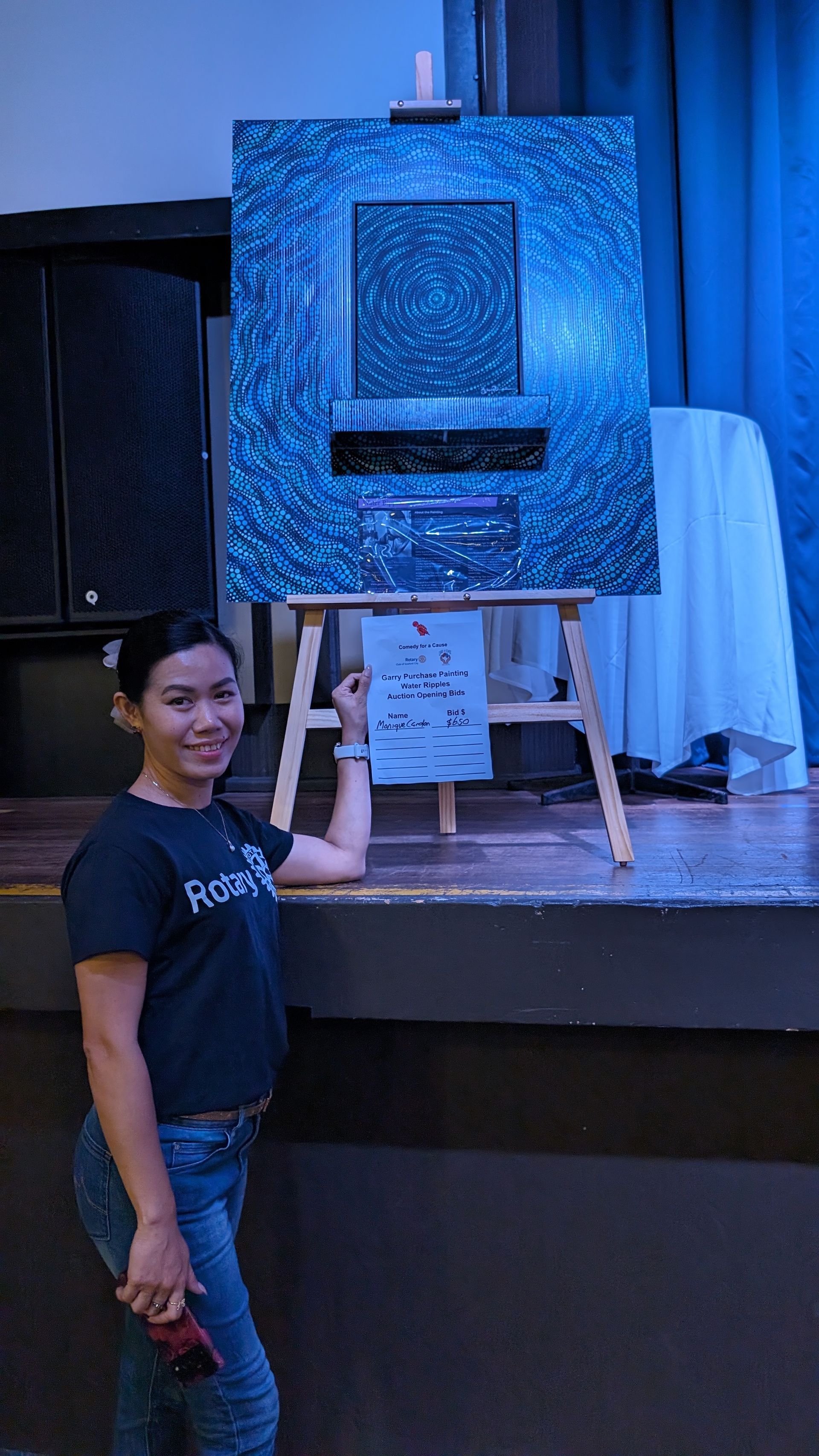 A woman is standing in front of a large painting on an easel.