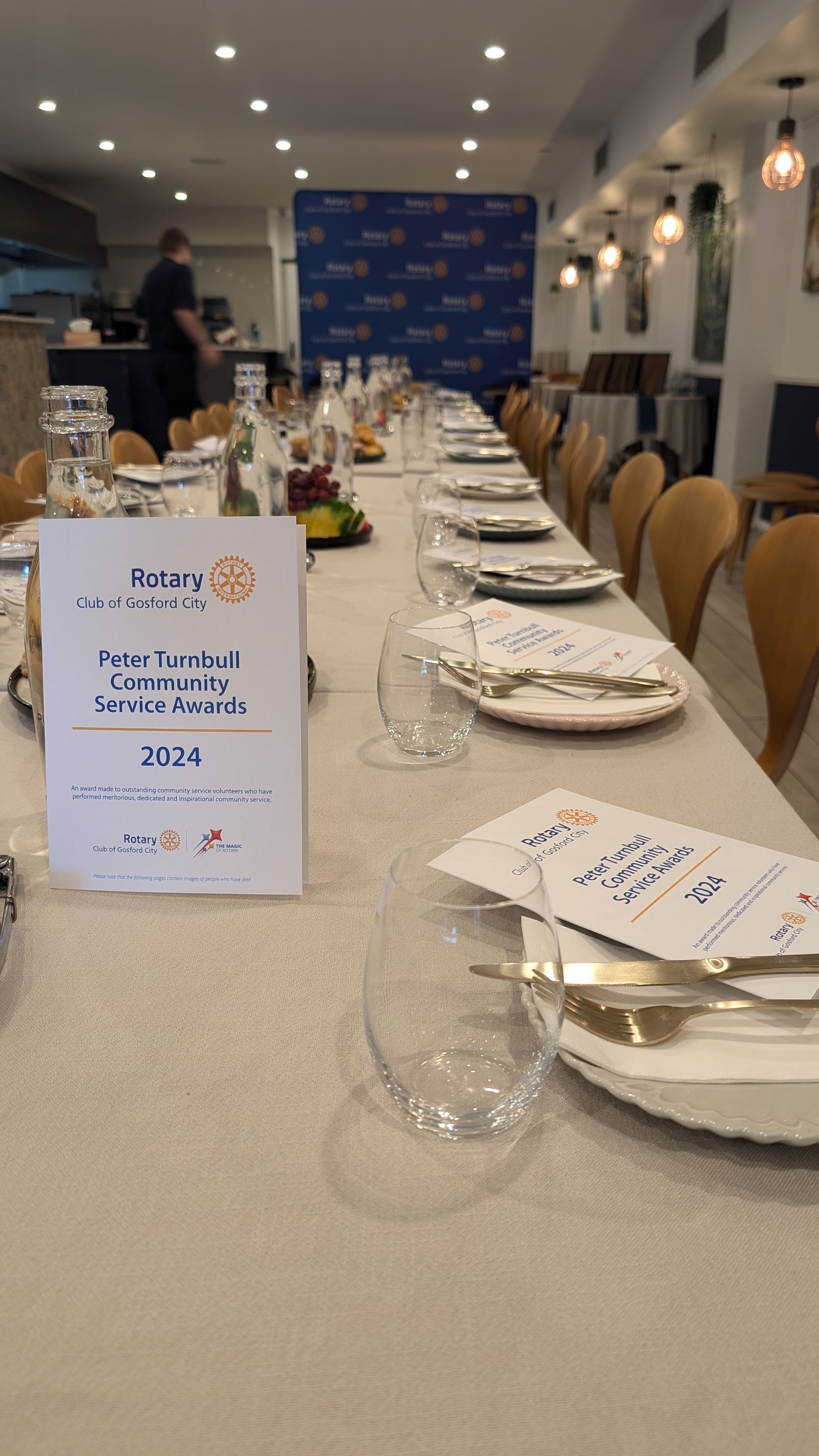 A long table with plates , glasses , utensils and a sign on it.