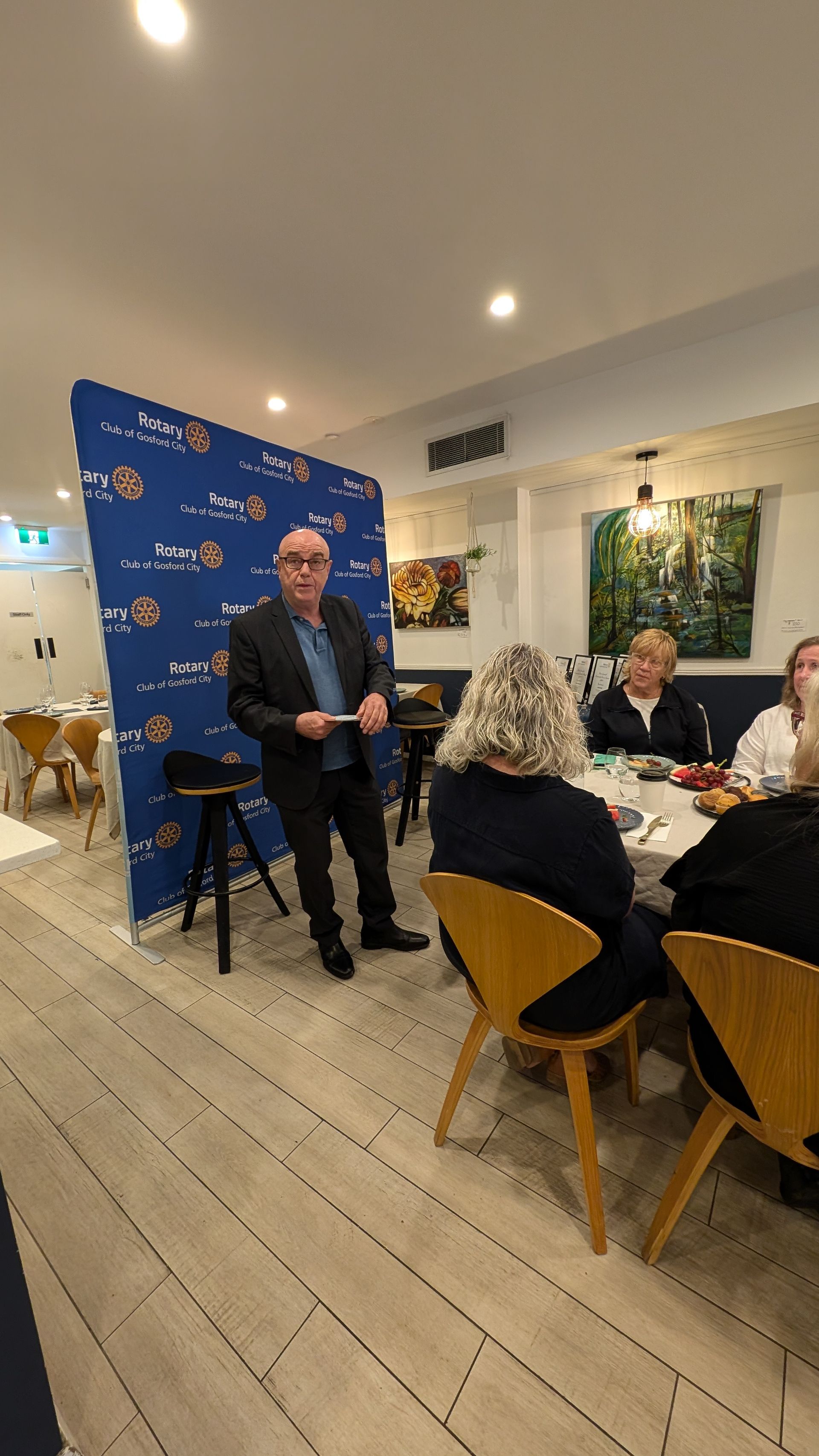 A man is standing in front of a group of people sitting at tables in a restaurant.