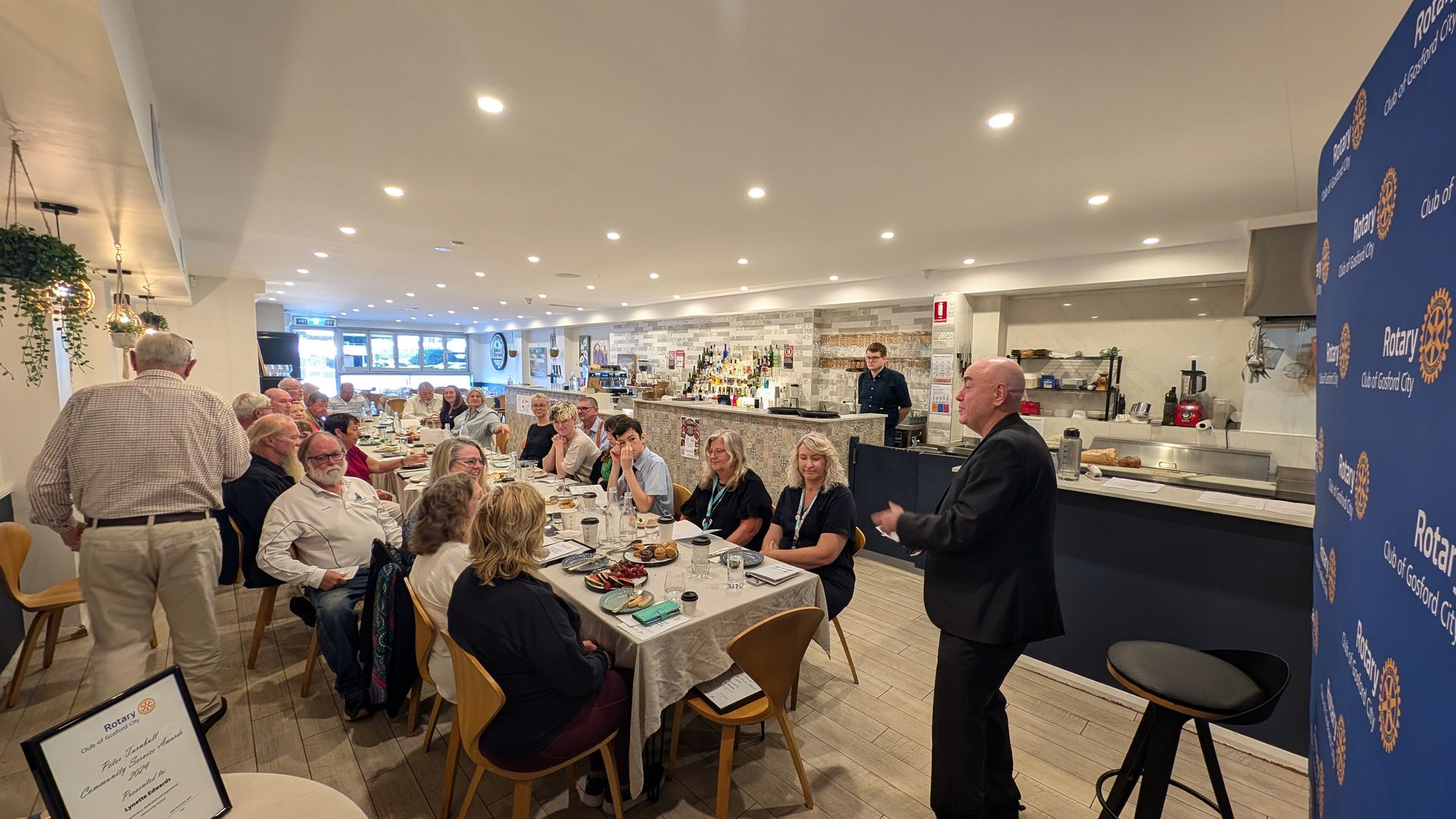 A man is giving a presentation to a group of people sitting at tables in a restaurant.