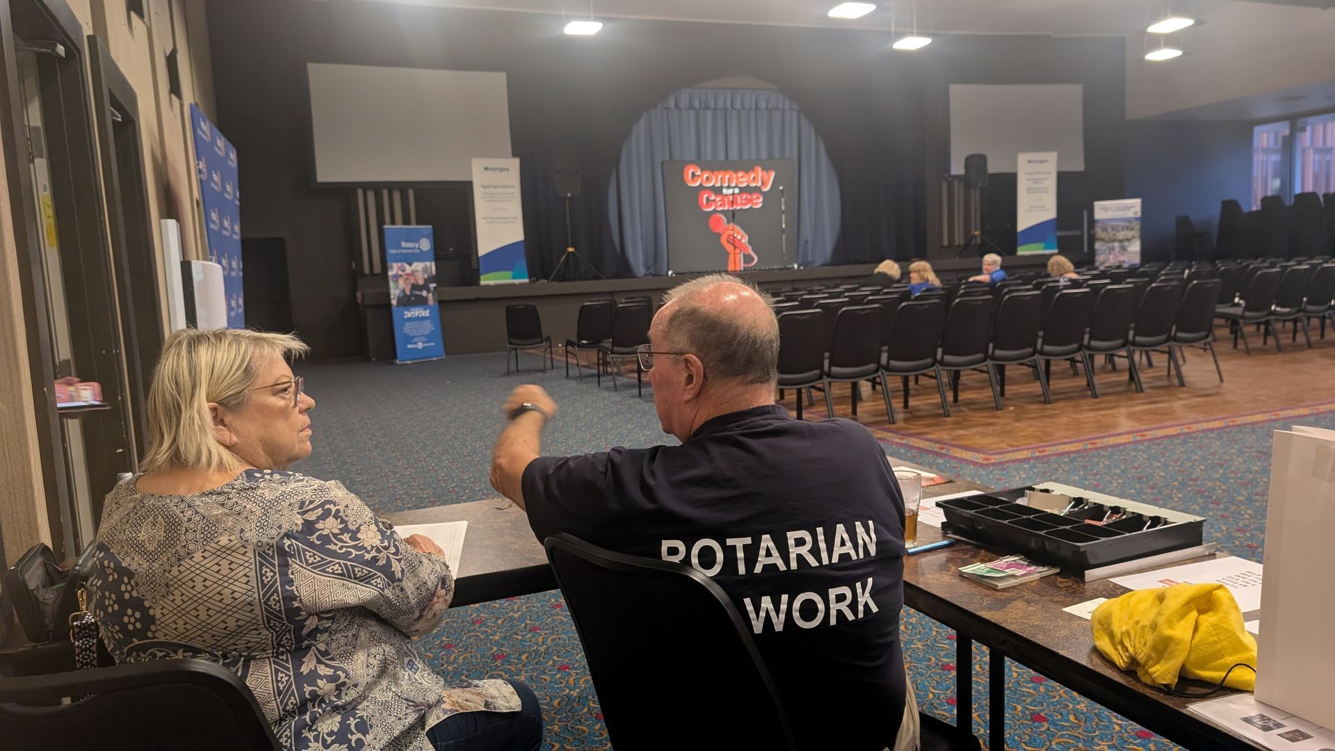 A man and a woman are sitting at a table in a large room.