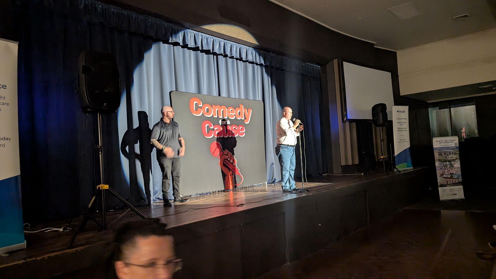 Two men are standing on a stage in front of a sign that says comedy club.
