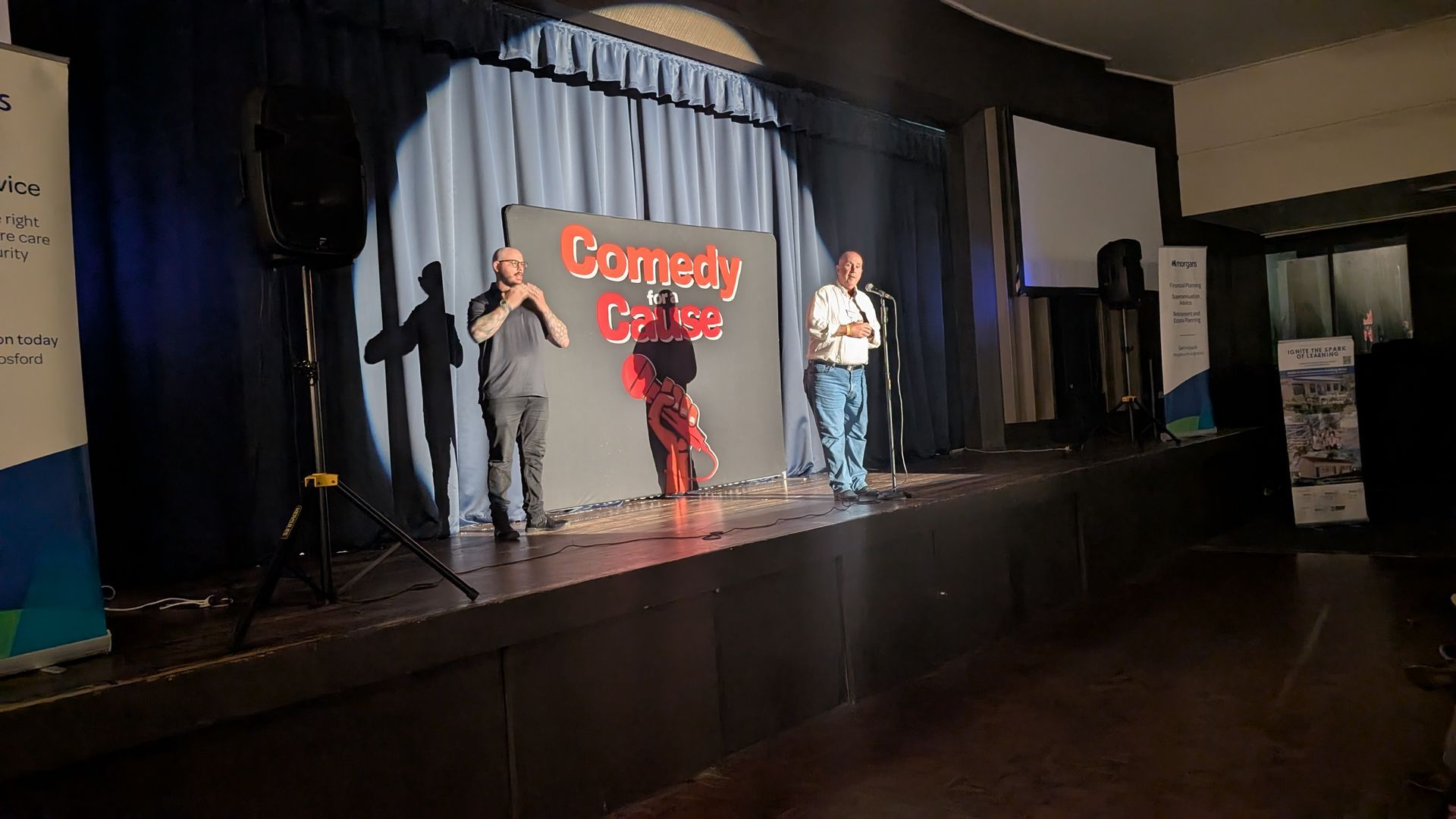 Two men are standing on a stage in front of a sign that says comedy palace.