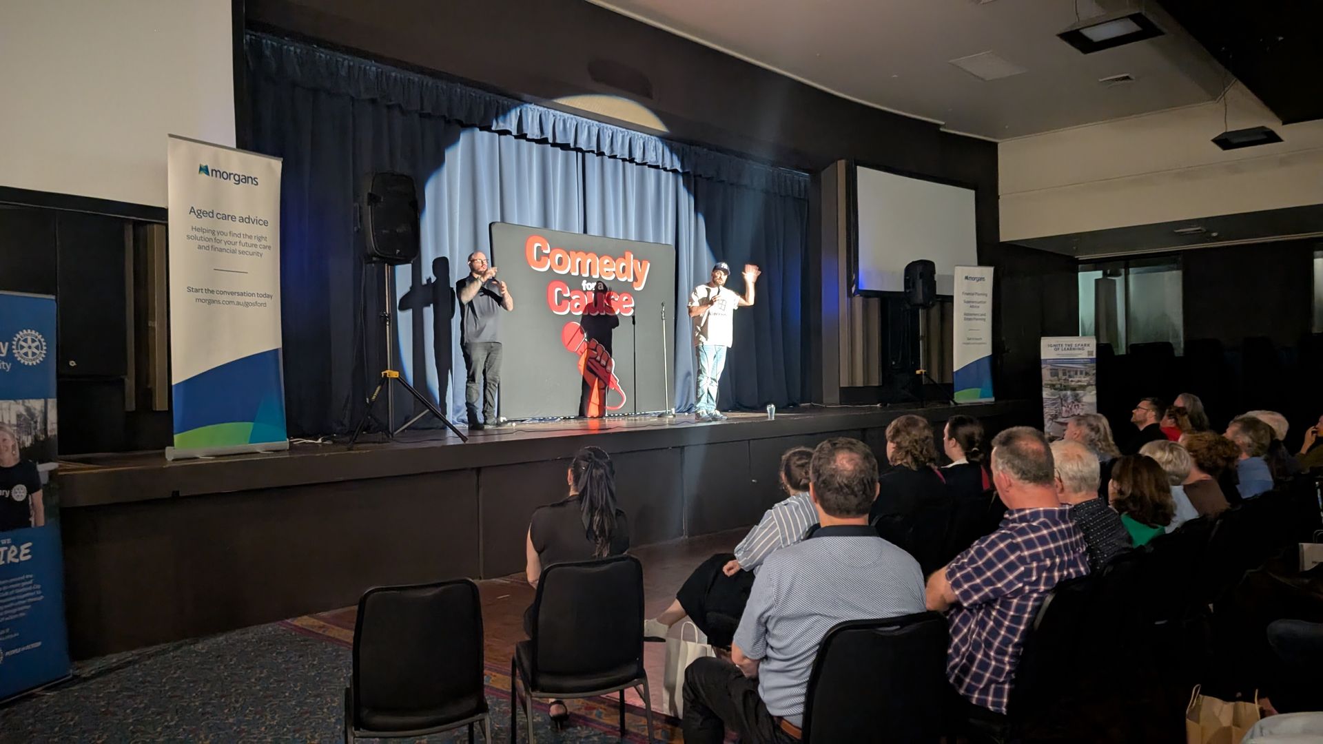A group of people are sitting in chairs in front of a stage watching a comedy show.